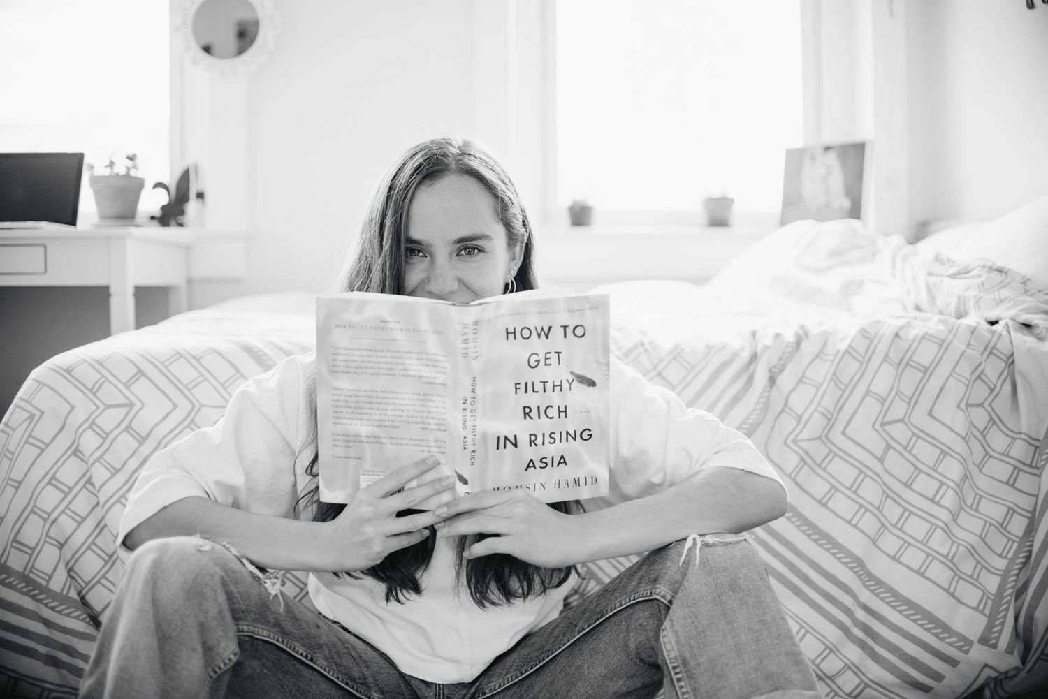 Black and white photo series showing someone reading a book while lying in bed with geometric patterned pillows.