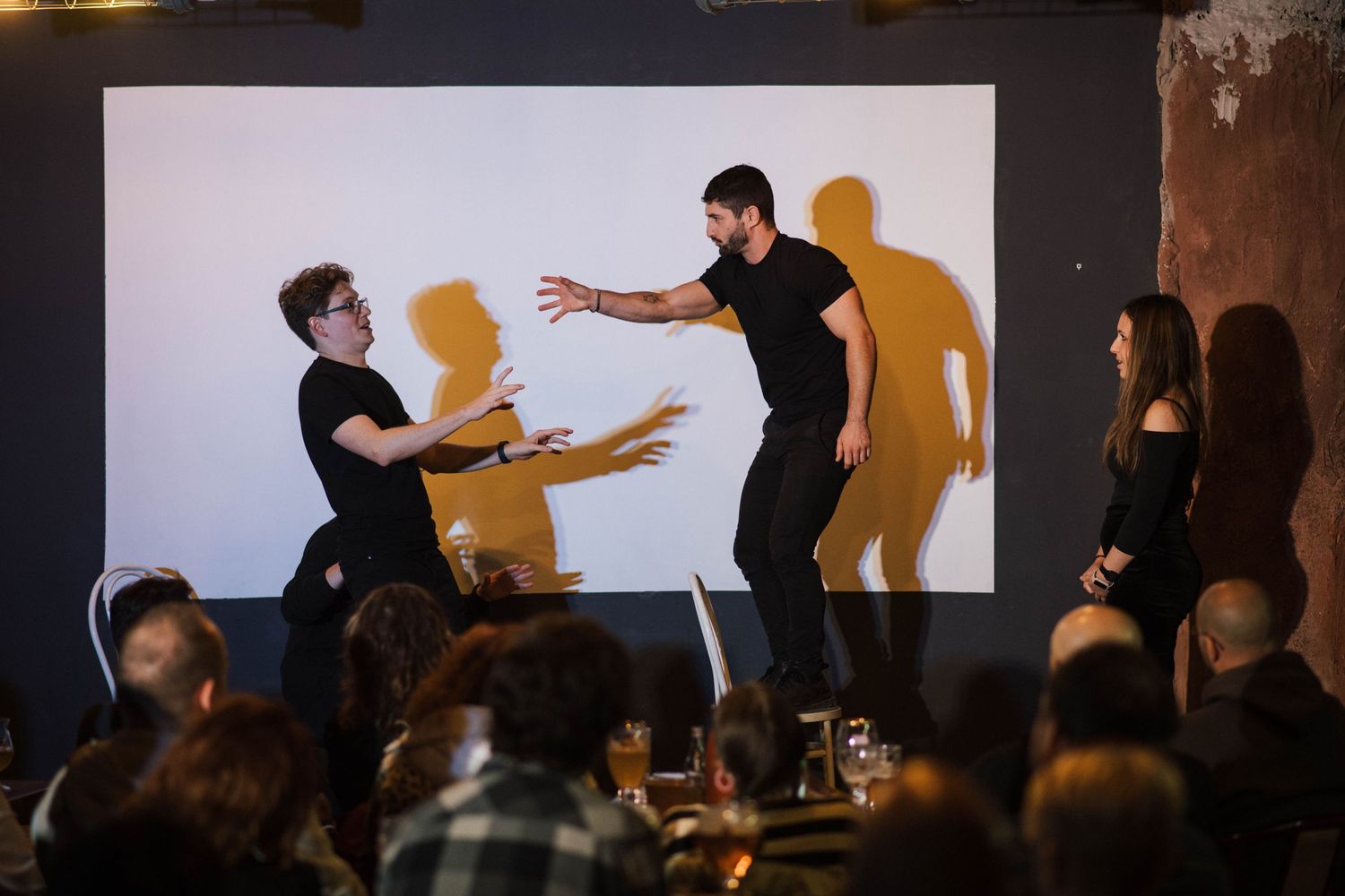 Performers on stage creating dramatic shadows against white backdrop.
