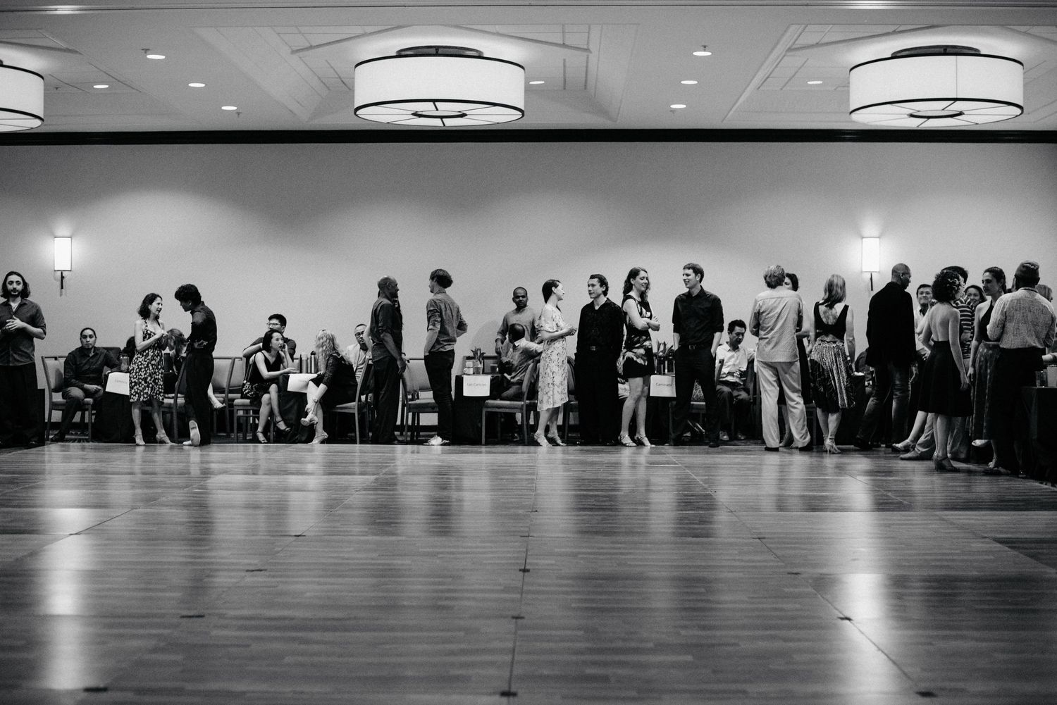 Long view of dancers practicing in a studio with overhead lighting.