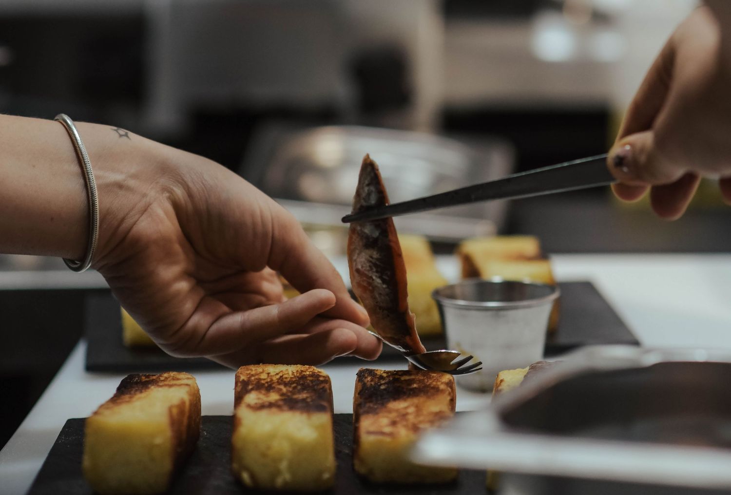 Chef slices fresh pineapple into thin pieces on wooden cutting board in professional kitchen.