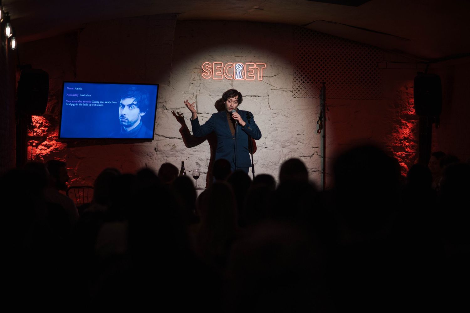 Performer on stage at a comedy club with dramatic blue and red lighting effects.