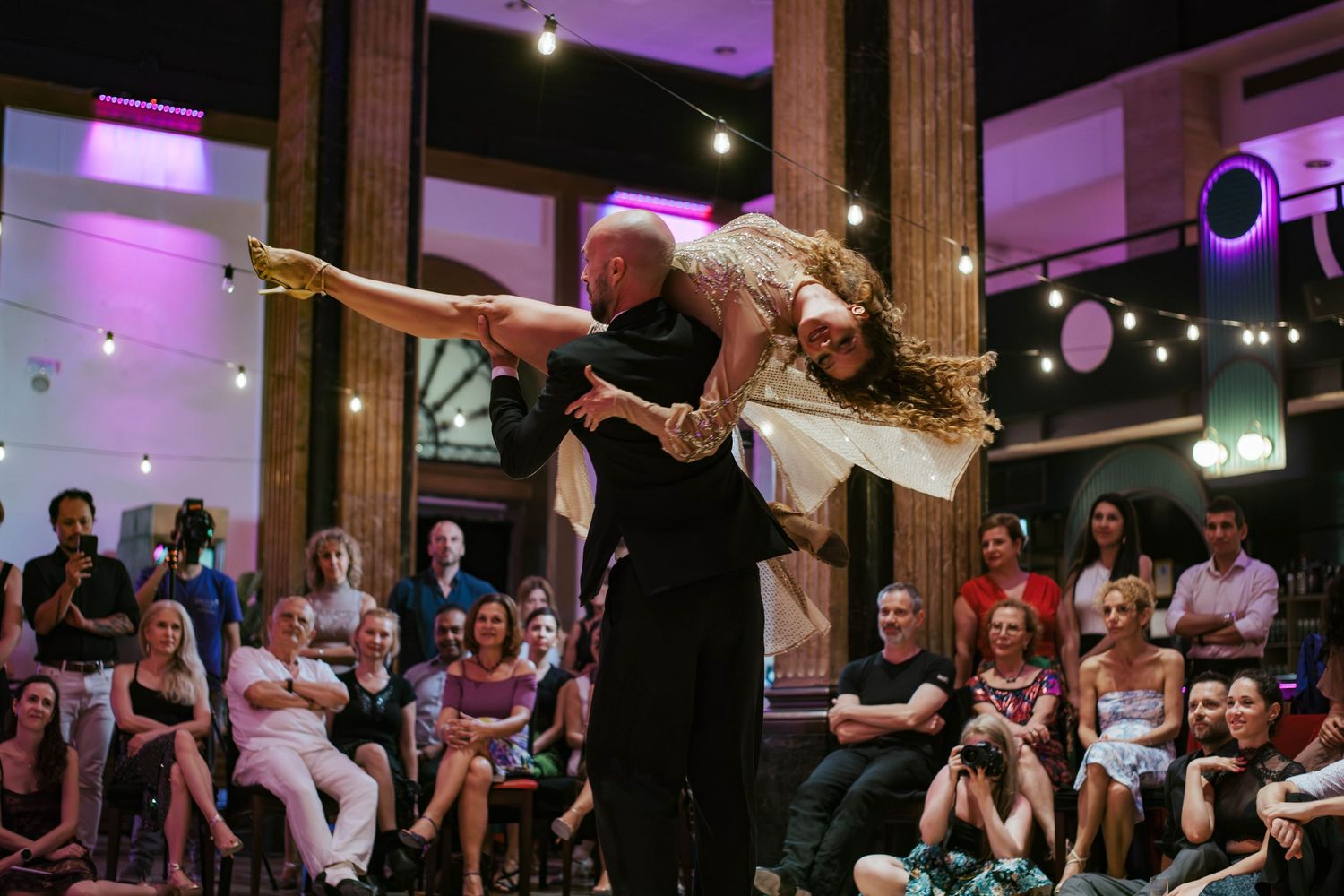 Social dance event with couples dancing in a venue illuminated by purple ambient lighting.