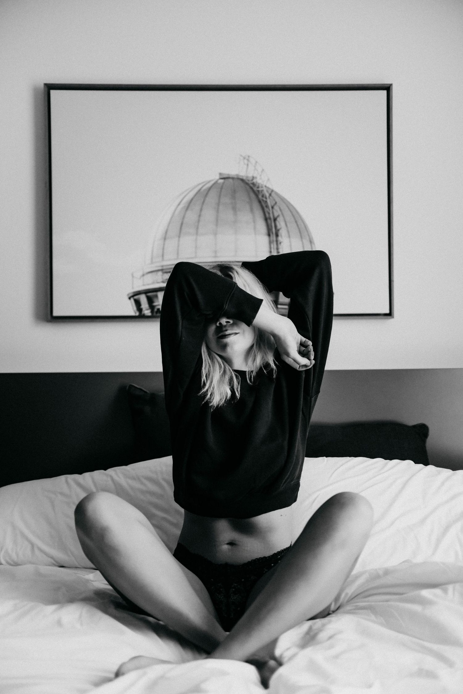 Artistic black and white portrait of person lying on white bedding.