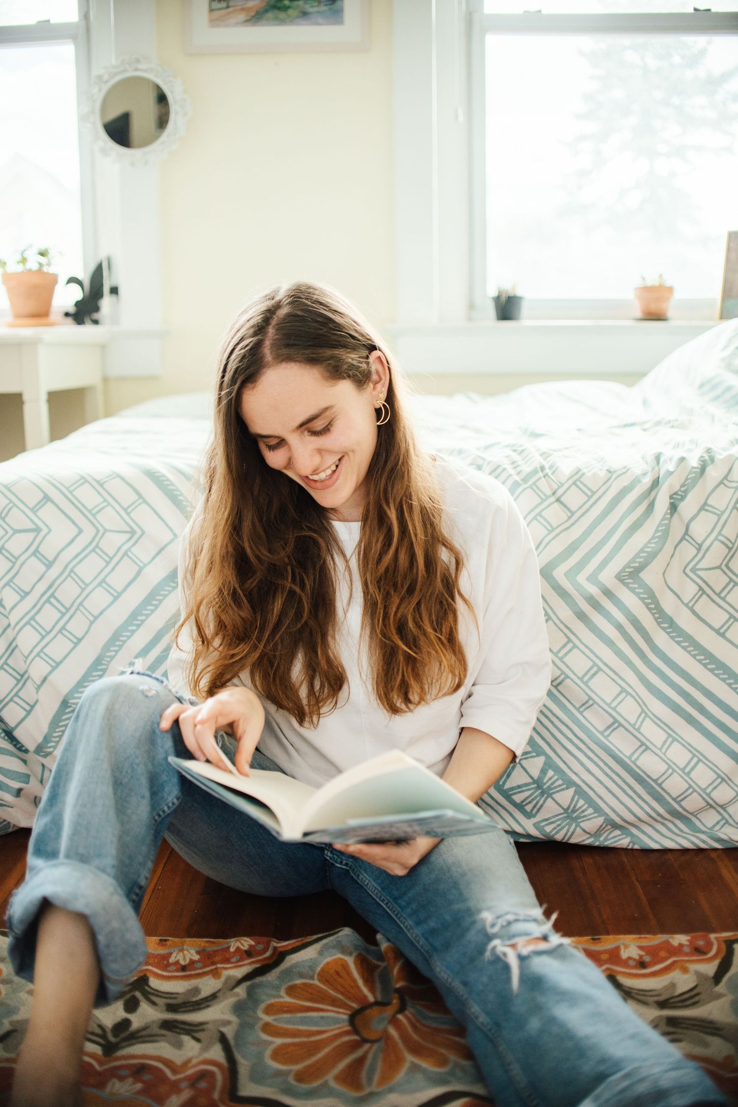Person relaxing on a couch while reading a book in a bright, modern living room with patterned pillows.