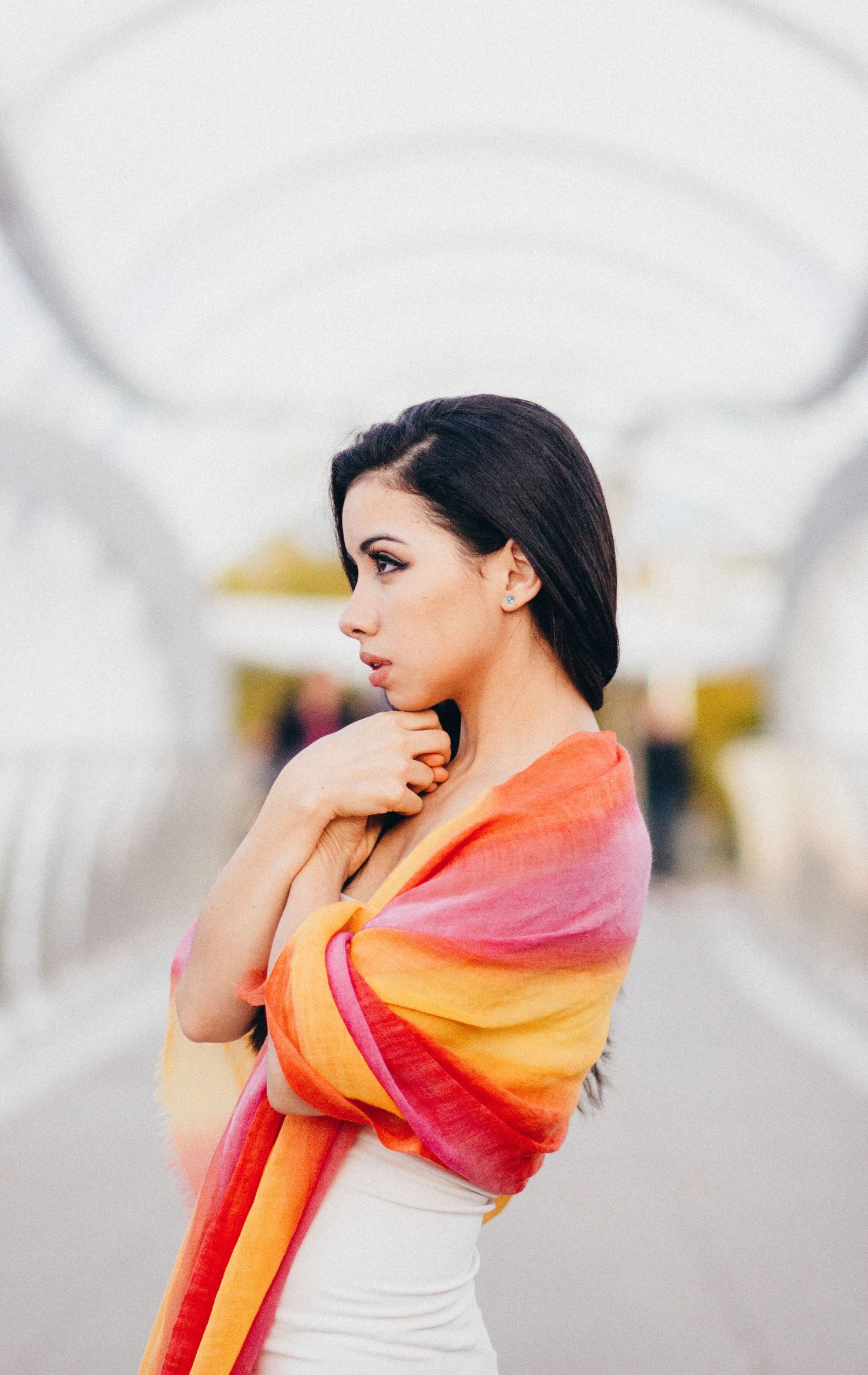 A woman in a white dress draped with a vibrant orange and pink ombre shawl poses against a blurred background.