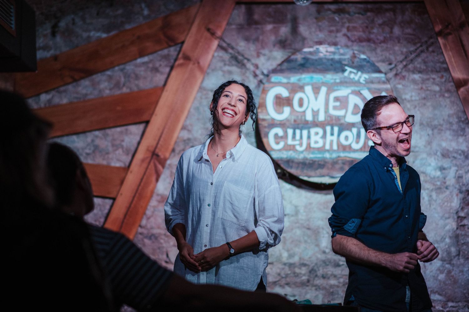 Comedy club interior with brick walls and stage lighting during a performance.