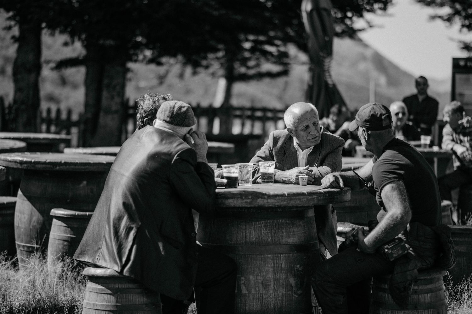 Vintage black and white photograph showing people gathered around a barrel table in an outdoor setting.