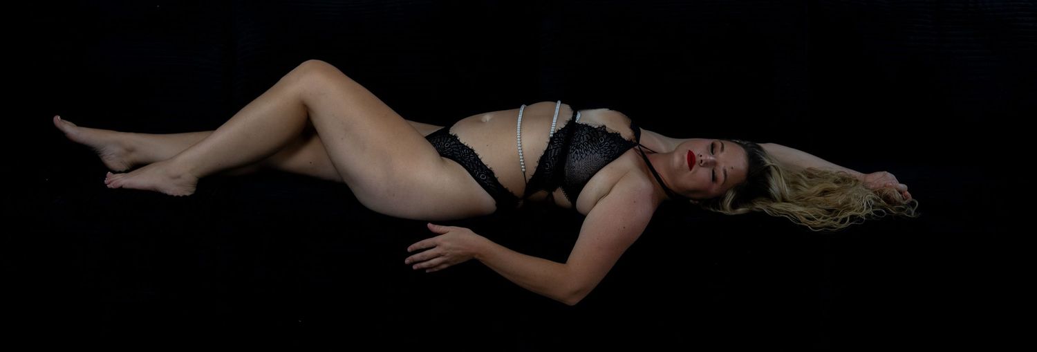 Woman in black lingerie posing gracefully against a dark background in a professional boudoir photo.