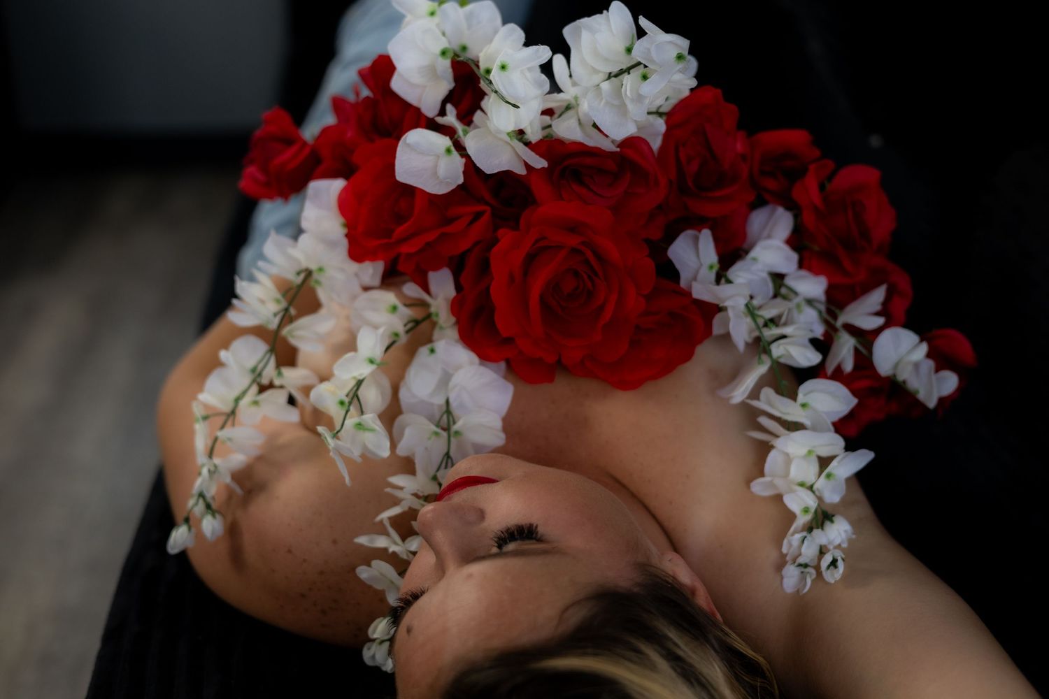 A woman lying down adorned with red roses and white flowers arranged beautifully across her chest and hair.