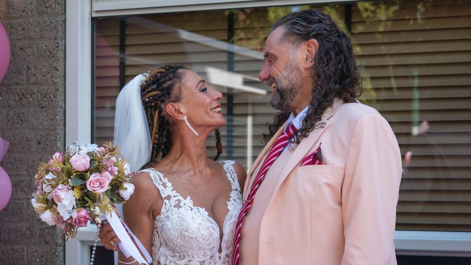 A couple shares a romantic moment during their outdoor wedding celebration in pink and white attire.