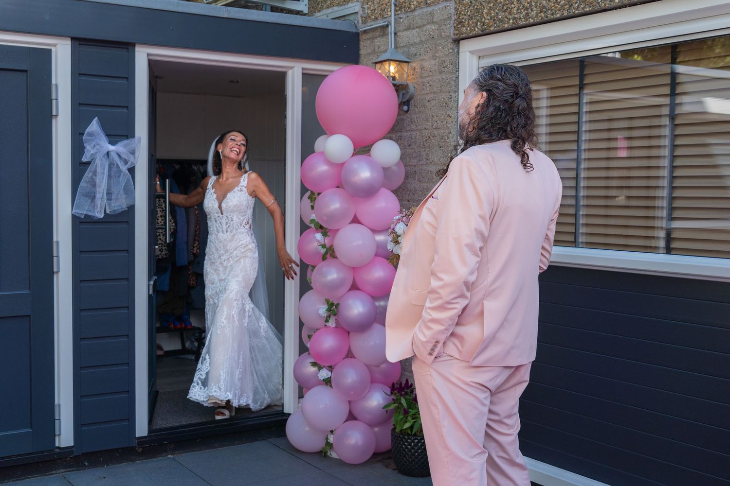 A pink balloon arch decorates an entrance with people in formal attire standing nearby for a special event celebration.