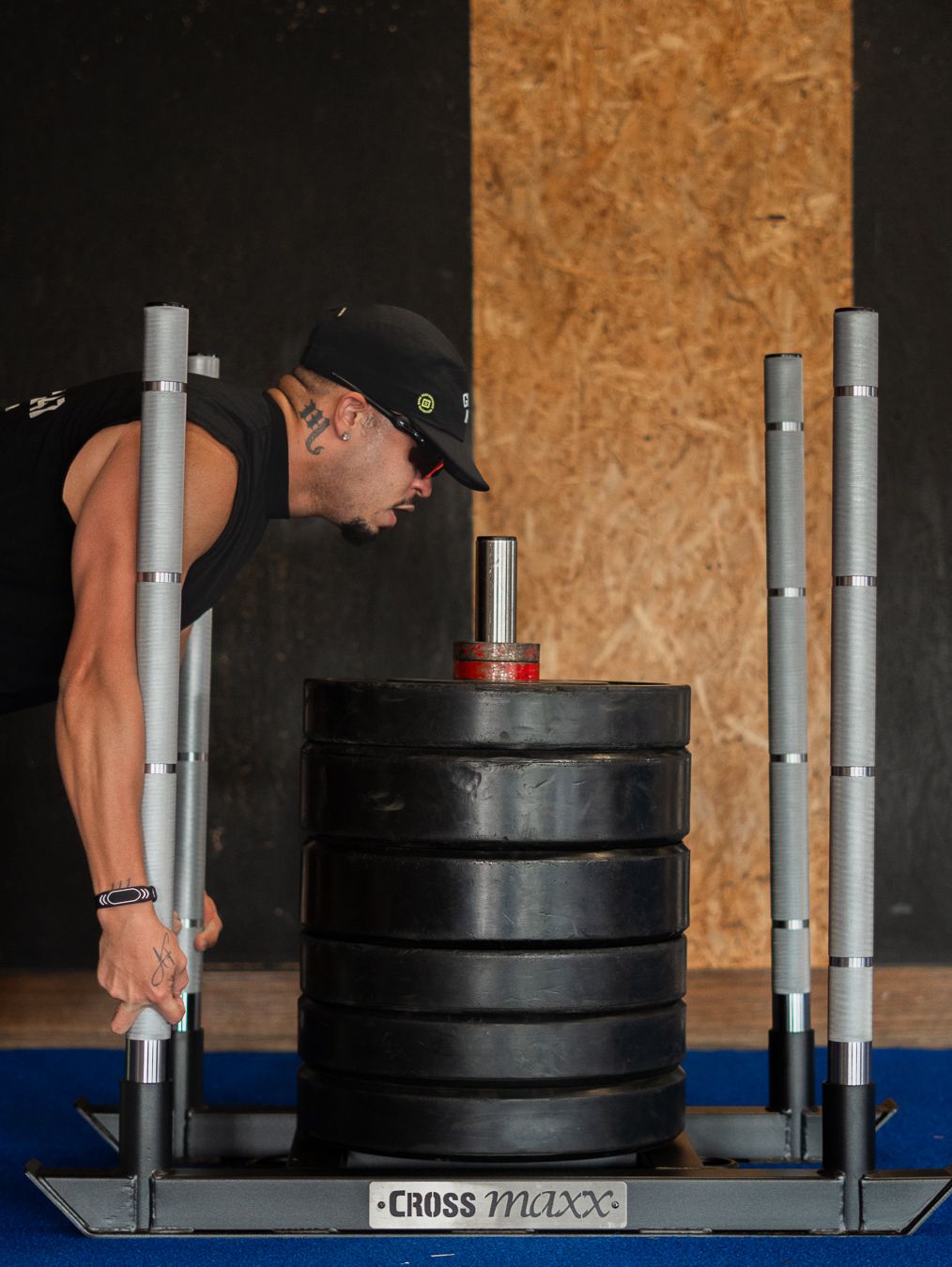 A person in a black cap performs a CrossFit workout with a heavy stack of weight plates on a specialized stand.