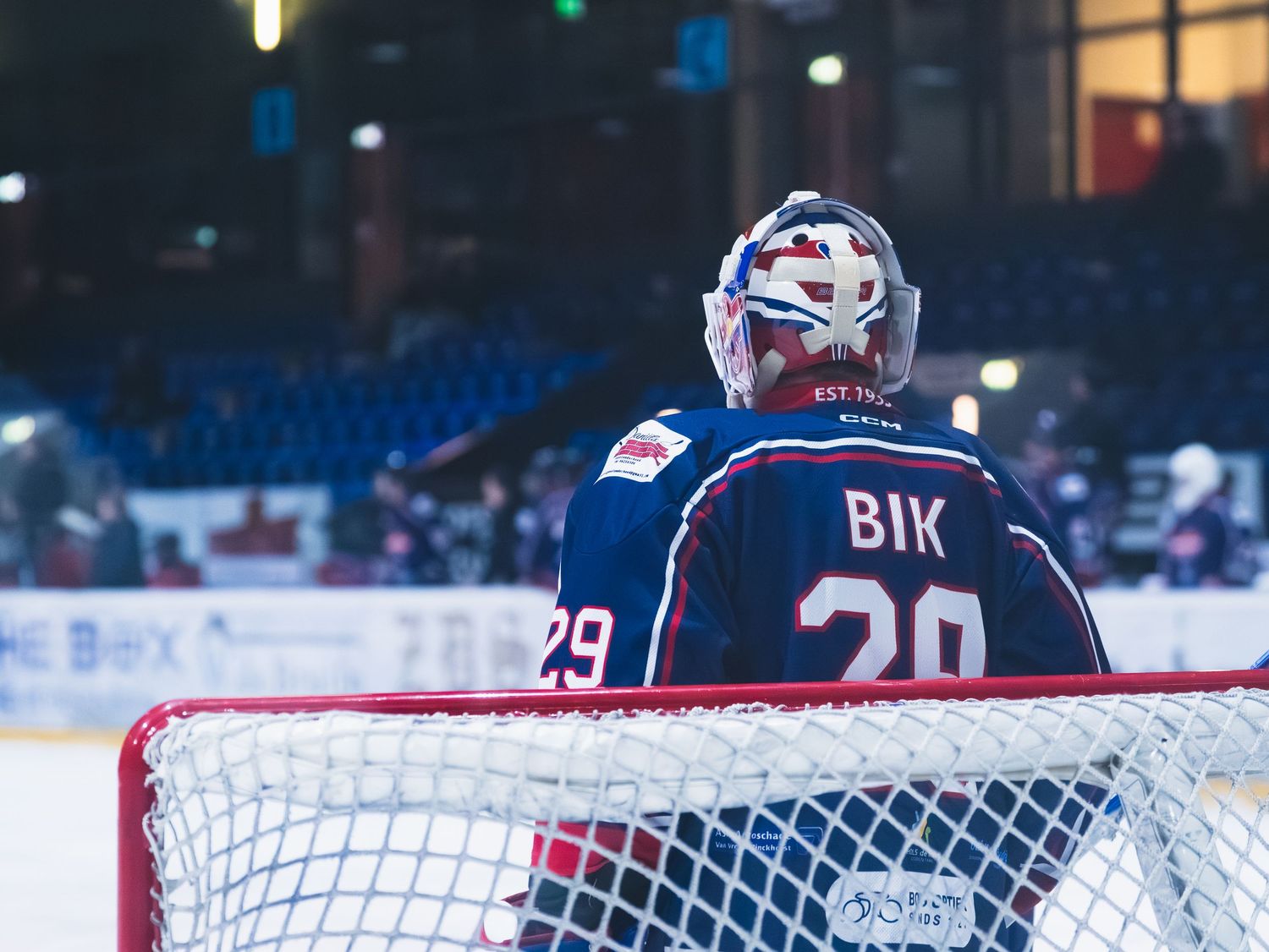A hockey goalie net and goal post visible on an ice rink during a game with blue lighting in the background.