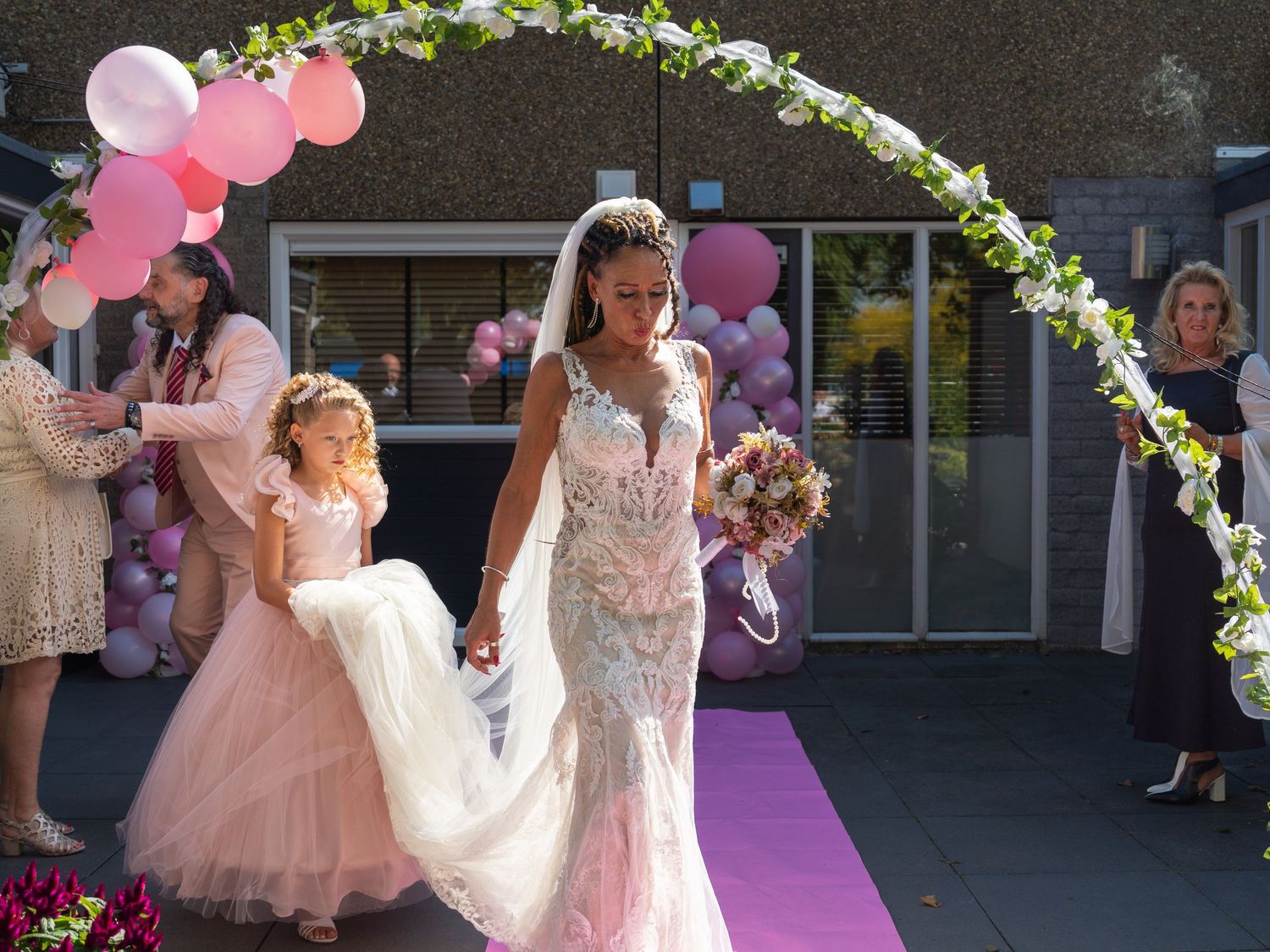 A floral arch decorated with pink balloons and white flowers creates an elegant outdoor wedding ceremony setting.