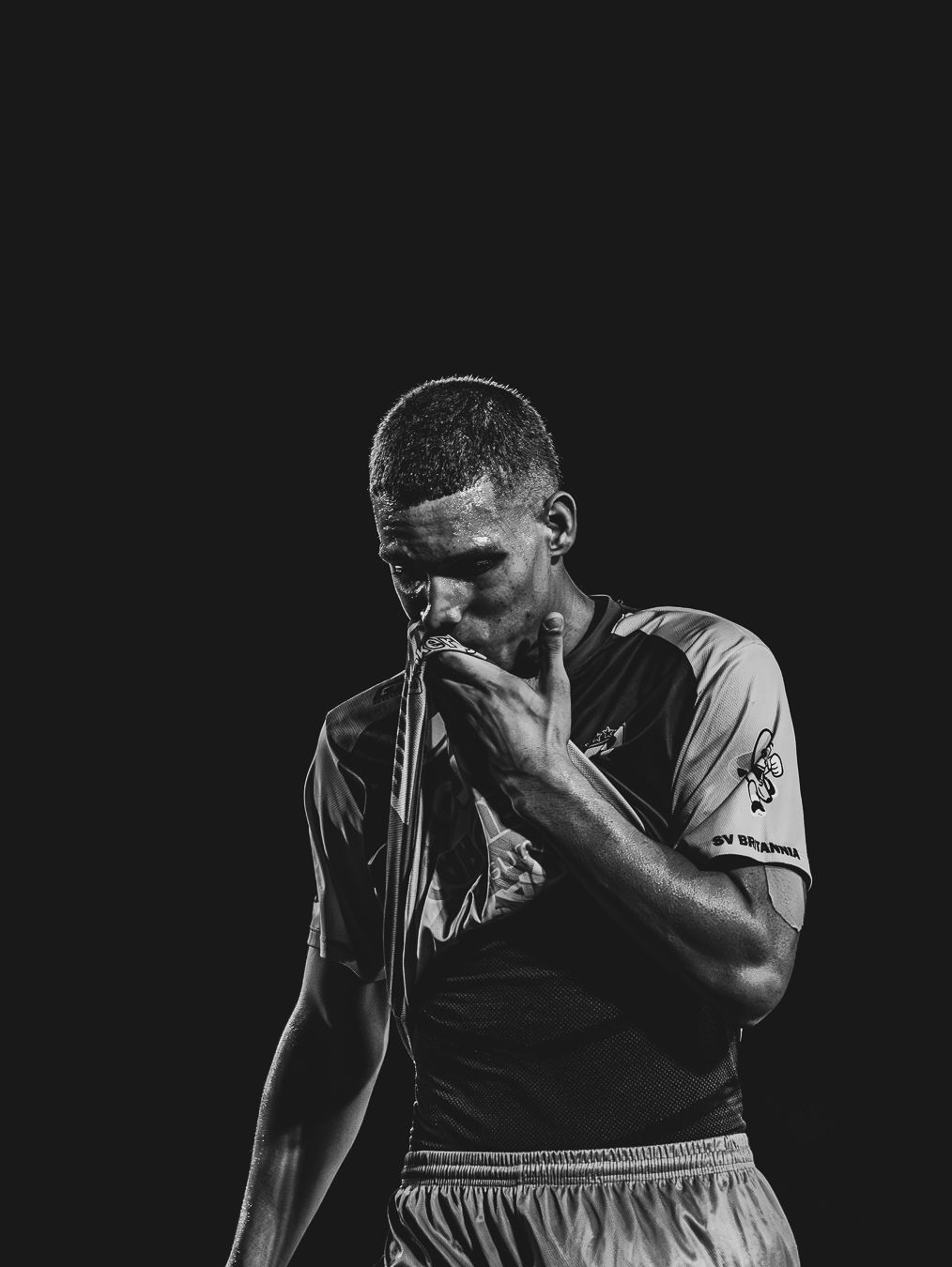Black and white photo of a male athlete in a sports jersey, head bowed, kissing his hands in a moment of emotion.