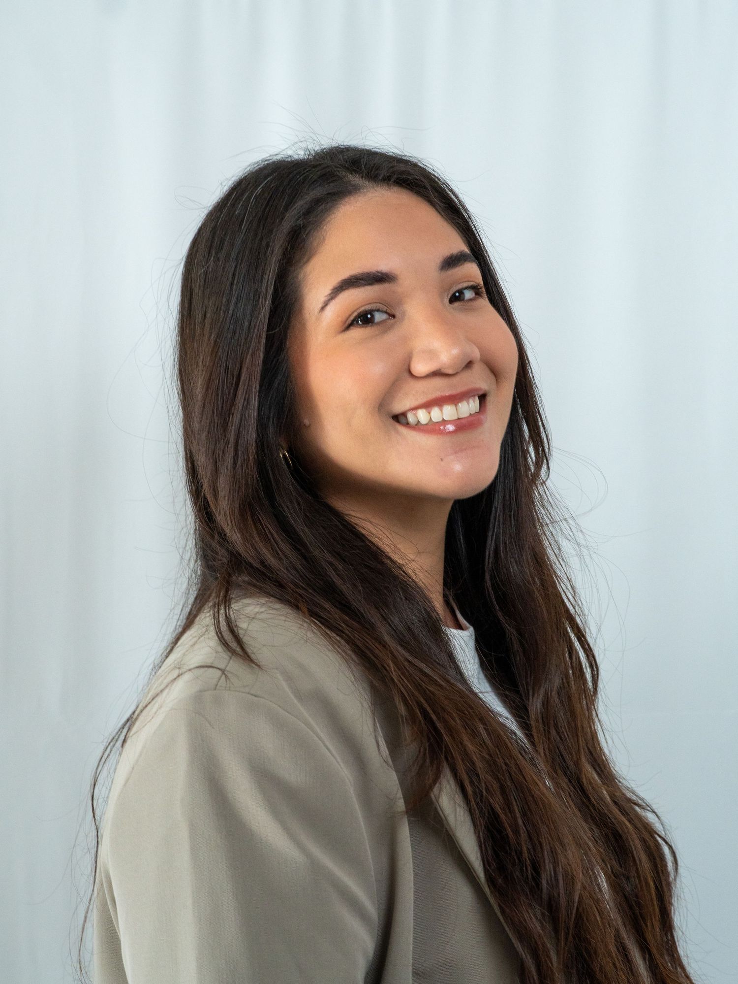 A series of four candid shots showing someone with long dark hair posing and smiling in a beige jacket against a light background.