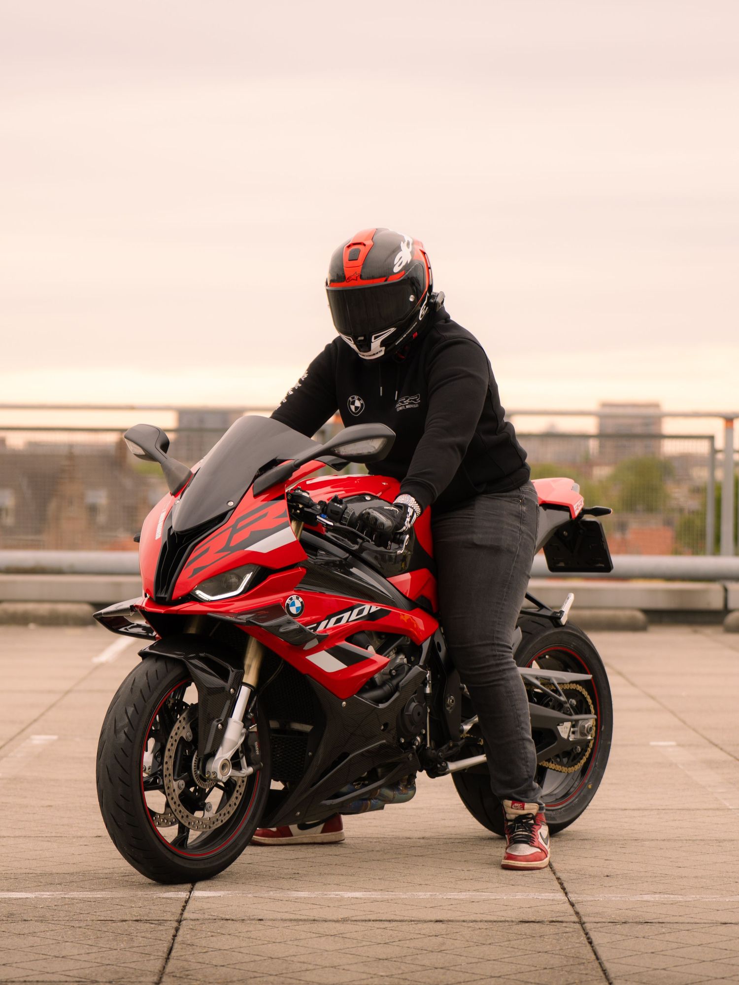 A red and black sports motorcycle is photographed from multiple angles on a rooftop parking area at sunset.