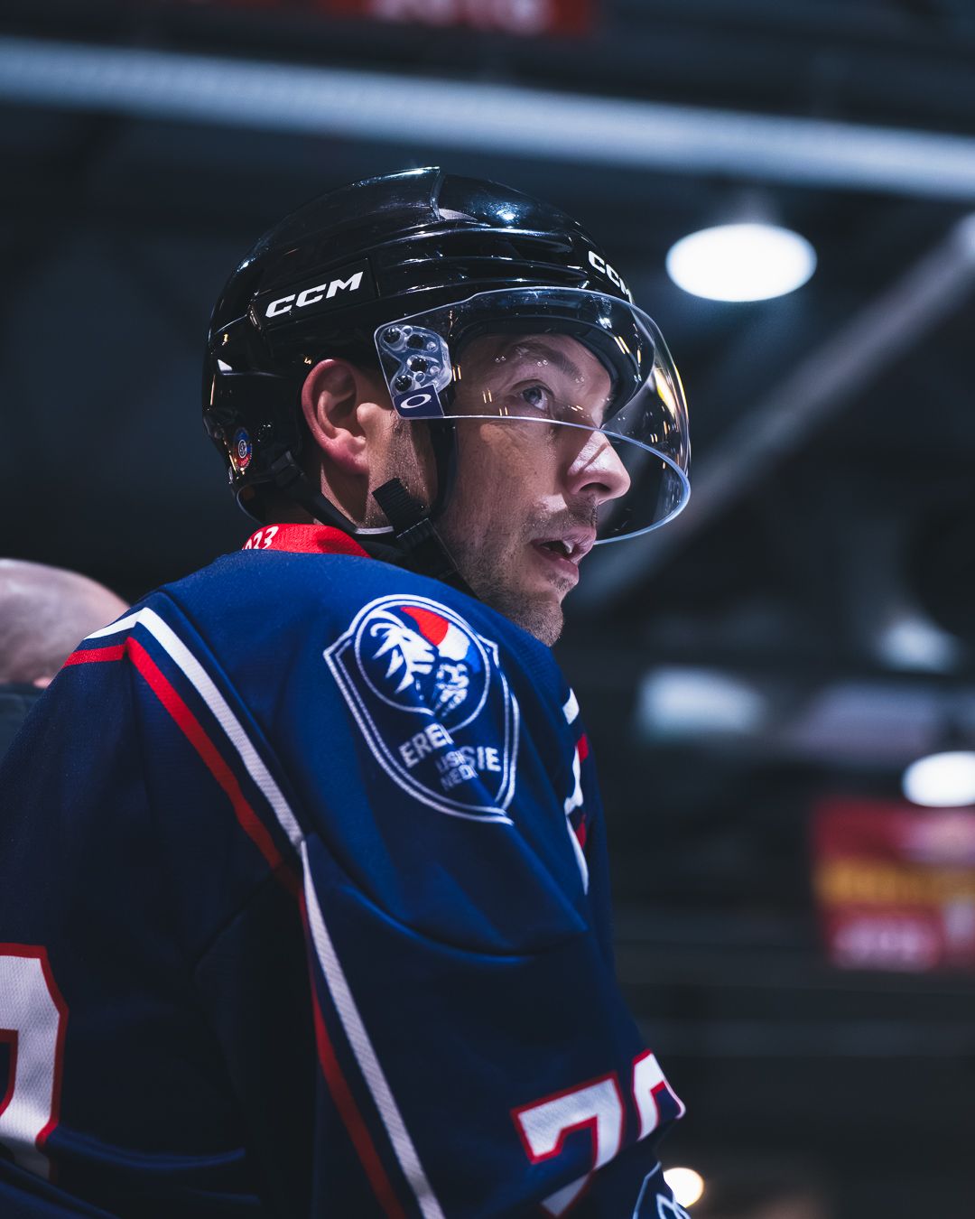 Hockey player wearing a blue and red jersey looks up at the scoreboard during a game.