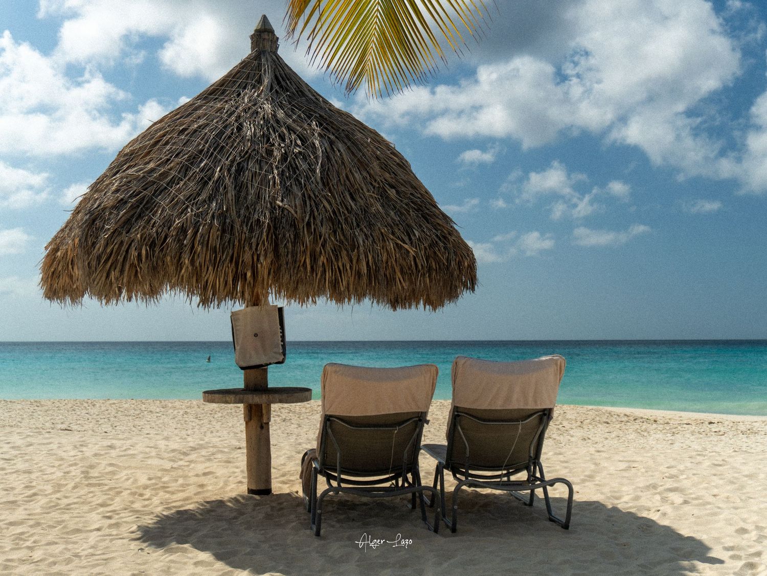 Two lounge chairs under a thatched palapa umbrella on a white sandy beach with turquoise ocean views.