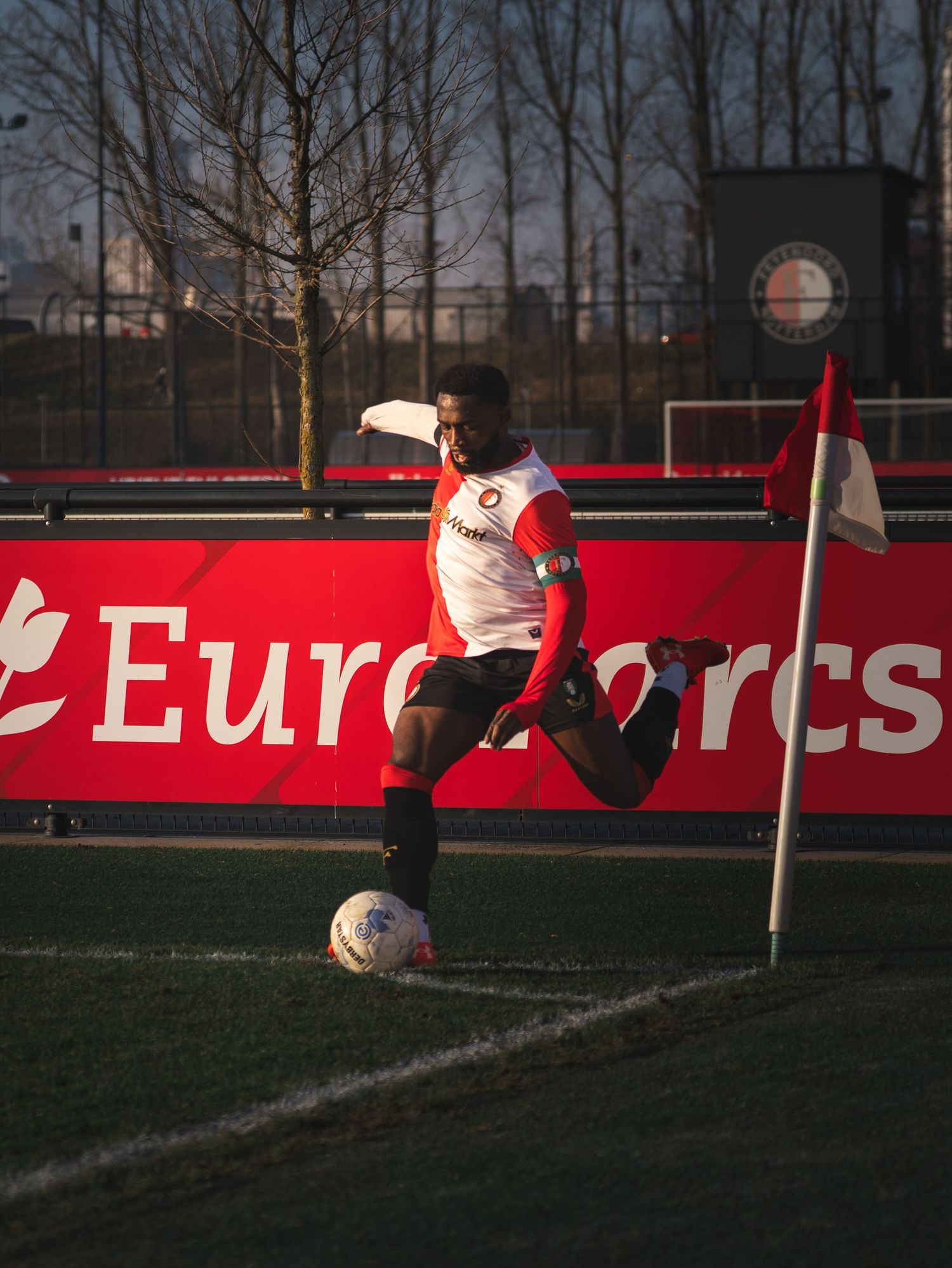 A soccer field with red advertising boards visible at dusk or dawn with trees silhouetted in the background.