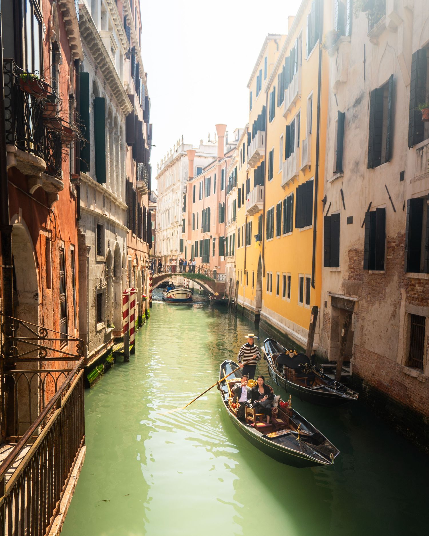A gondolier navigates a narrow Venice canal lined with colorful historic buildings on a sunny day.