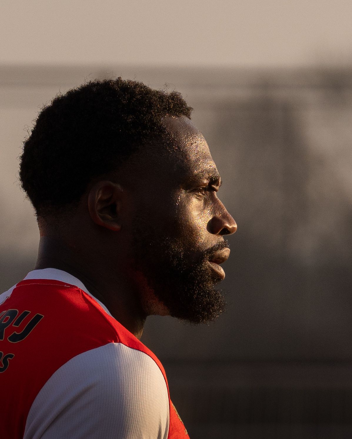 Profile view of an athlete in a red jersey with a full beard looking off into the distance at sunset.