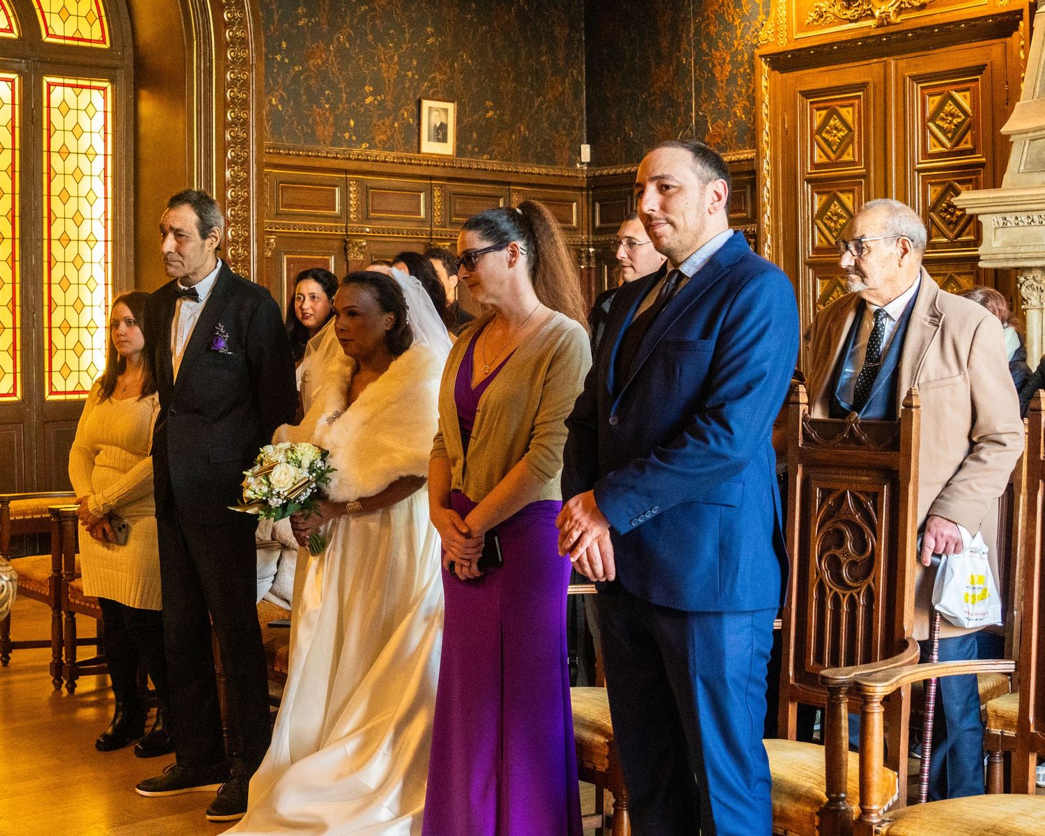 Wedding party and guests standing in a beautifully decorated wooden room with stained glass windows.