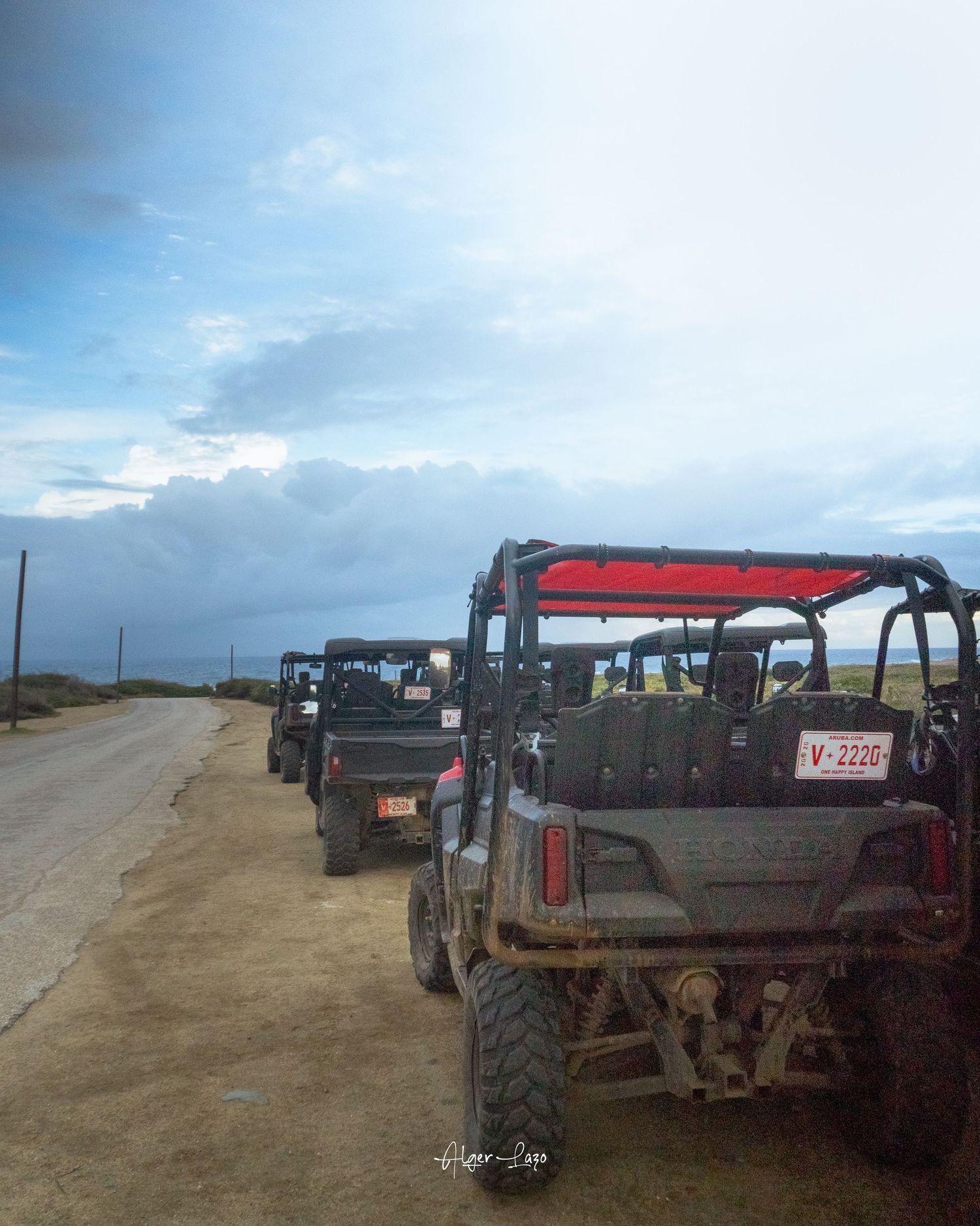 A convoy of off-road jeeps parked along a coastal road under a dramatic cloudy sky.