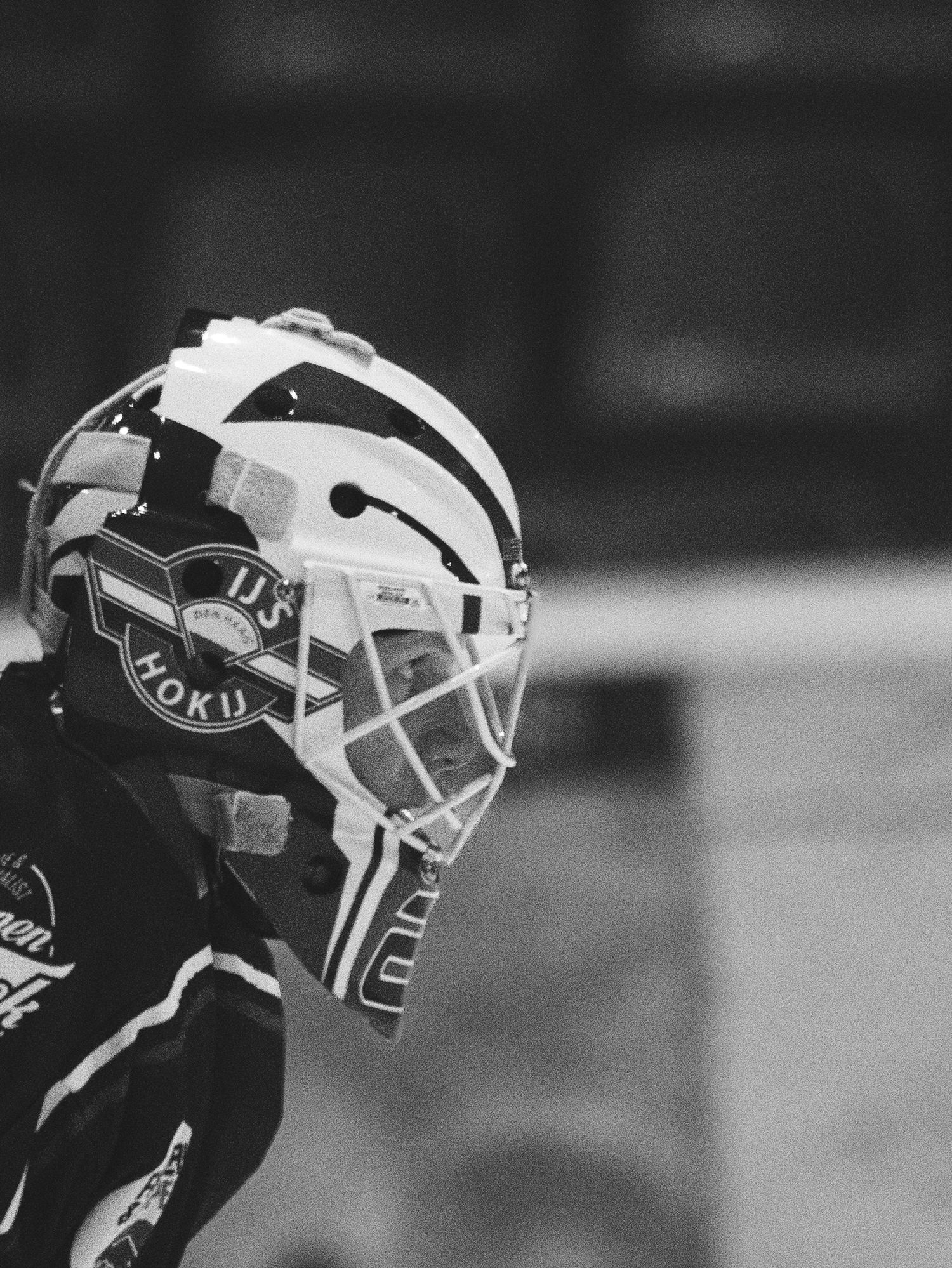 A black and white close-up of a hockey goalie mask with dramatic lighting and contrasting shadows.