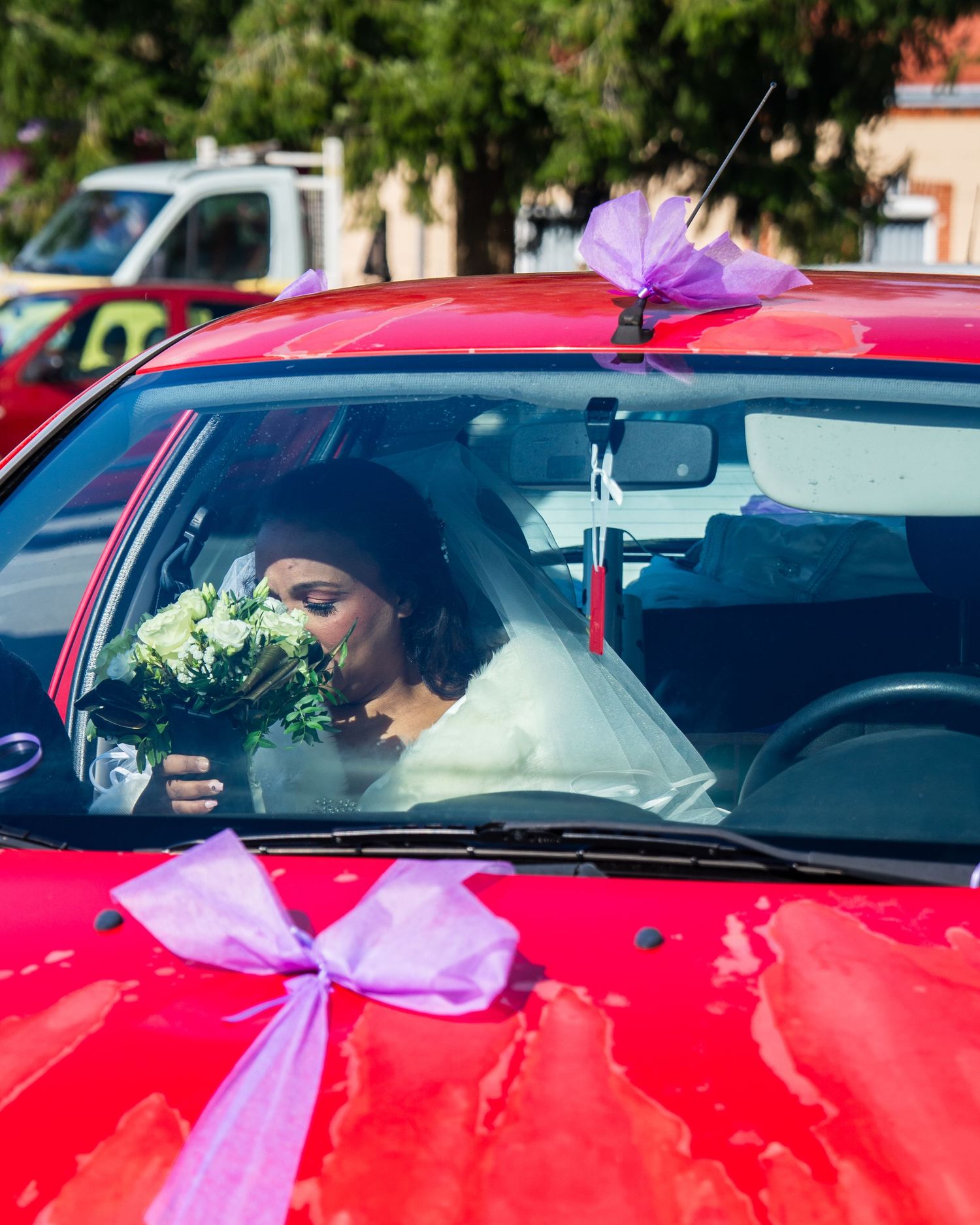 A red car decorated with purple bows for a wedding celebration, with a bouquet visible through the windshield.