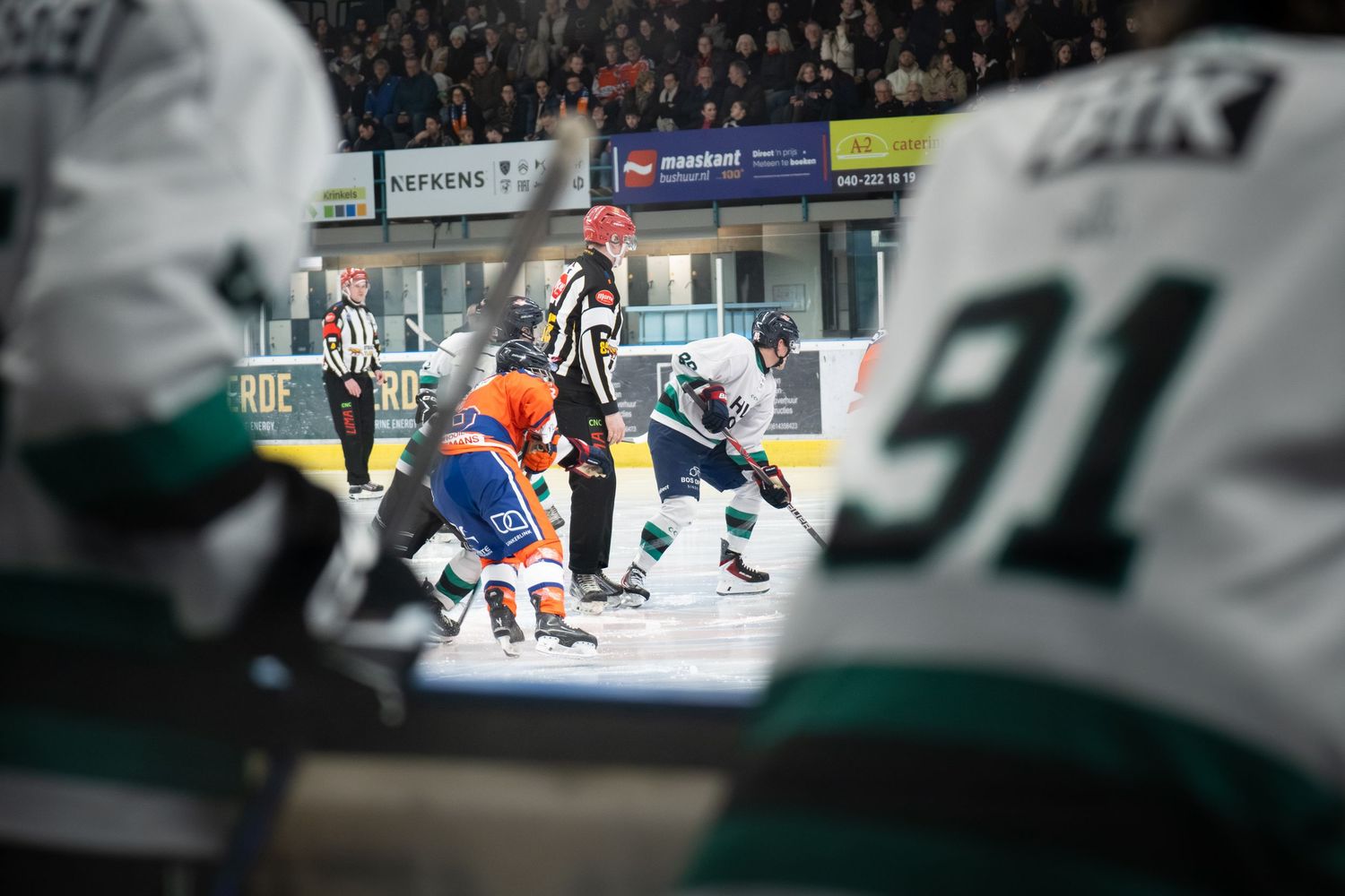 Hockey players in action during a game with orange and blue jerseys competing on the ice.