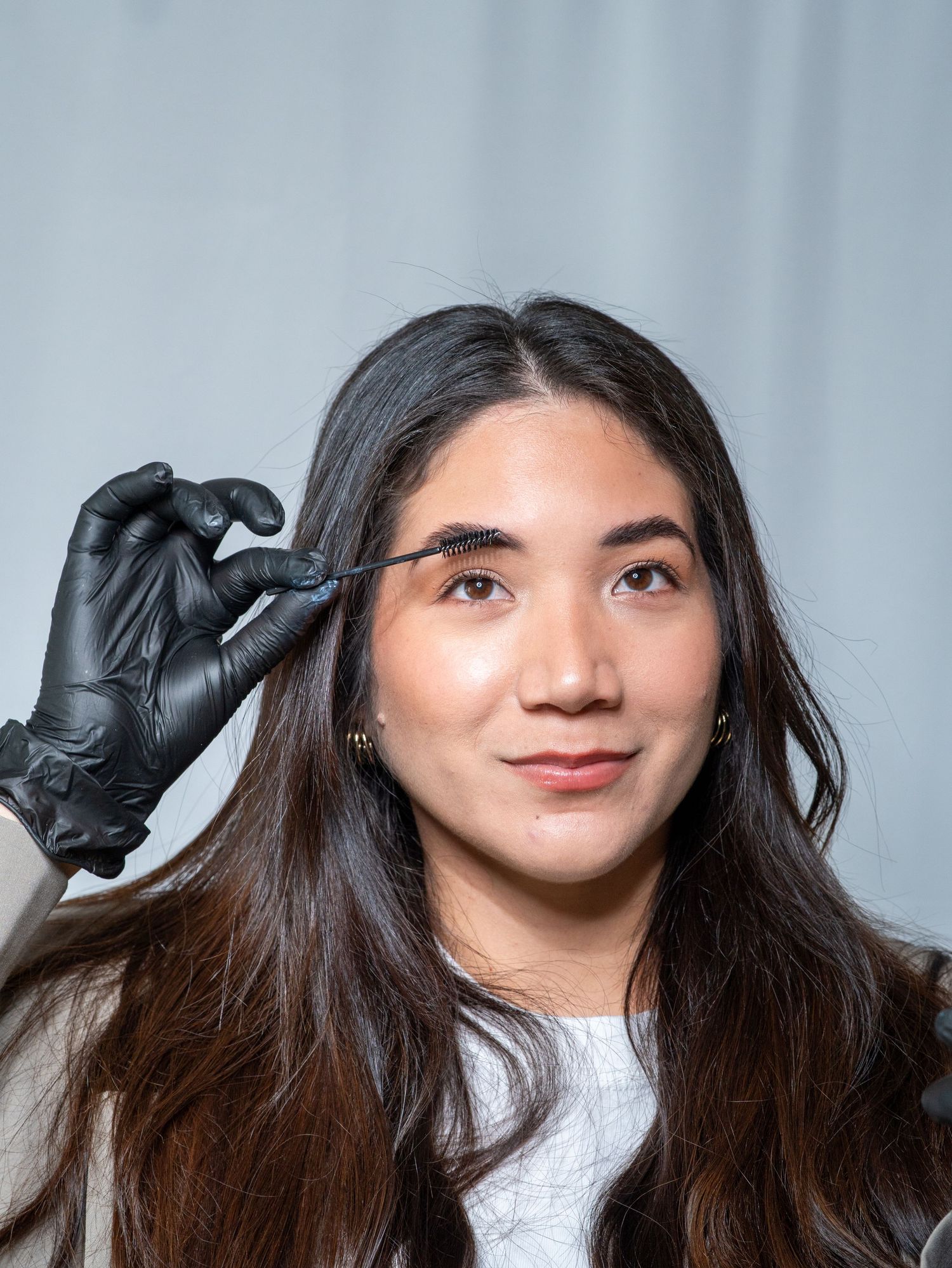 A series of four photos showing someone with long dark hair putting on black latex gloves against a light background.