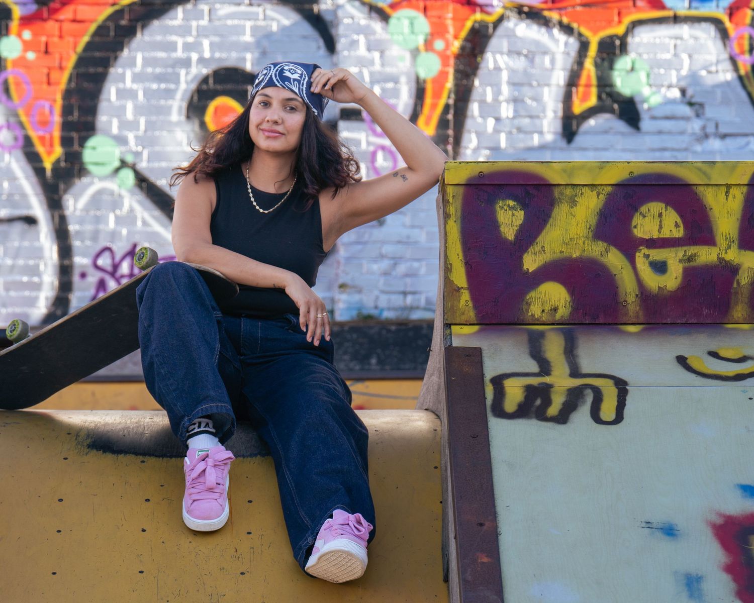 A series of five similar photos showing someone sitting against a graffiti wall wearing a black tank top and pink shoes.