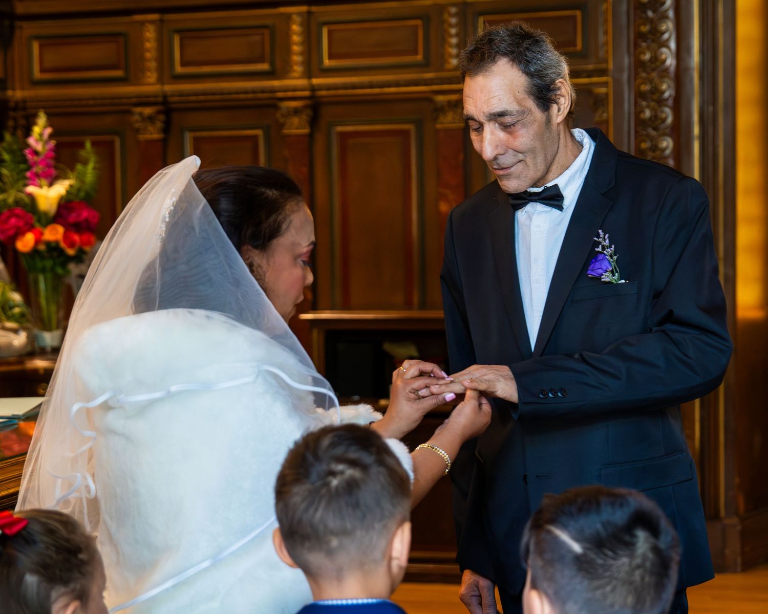 A wedding ceremony moment shows exchange of rings in an ornate wooden church interior.