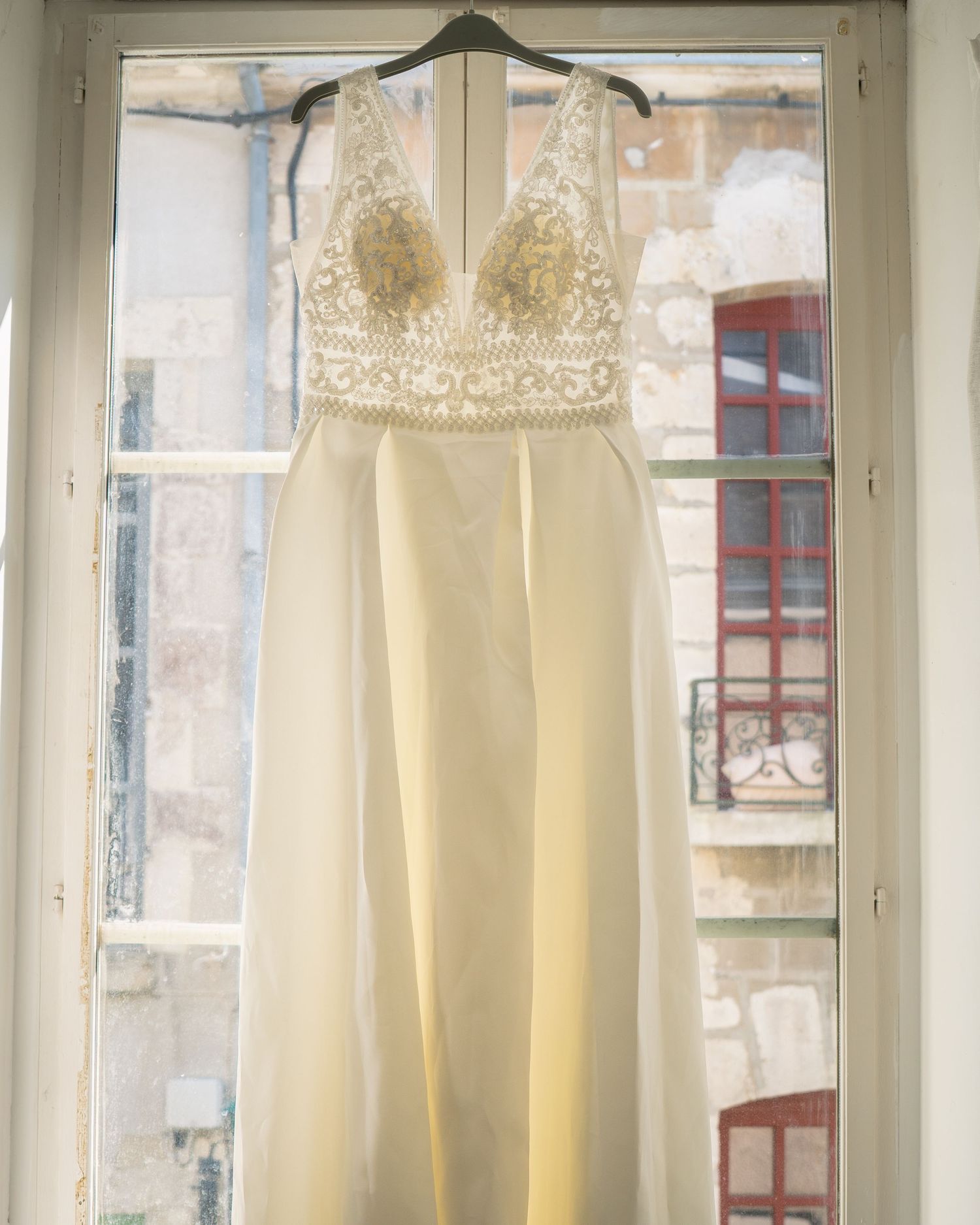 White lace wedding dresses hanging on display in a bridal boutique with vintage-style windows in the background.