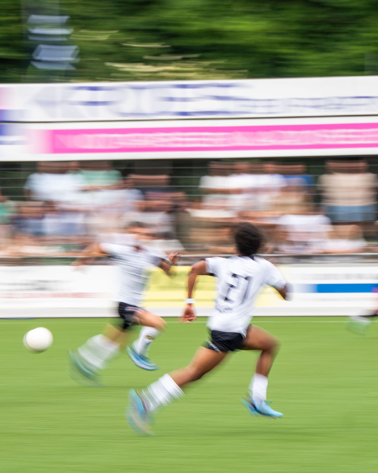 Motion blur effect shows soccer players running on green grass field during competitive match action.