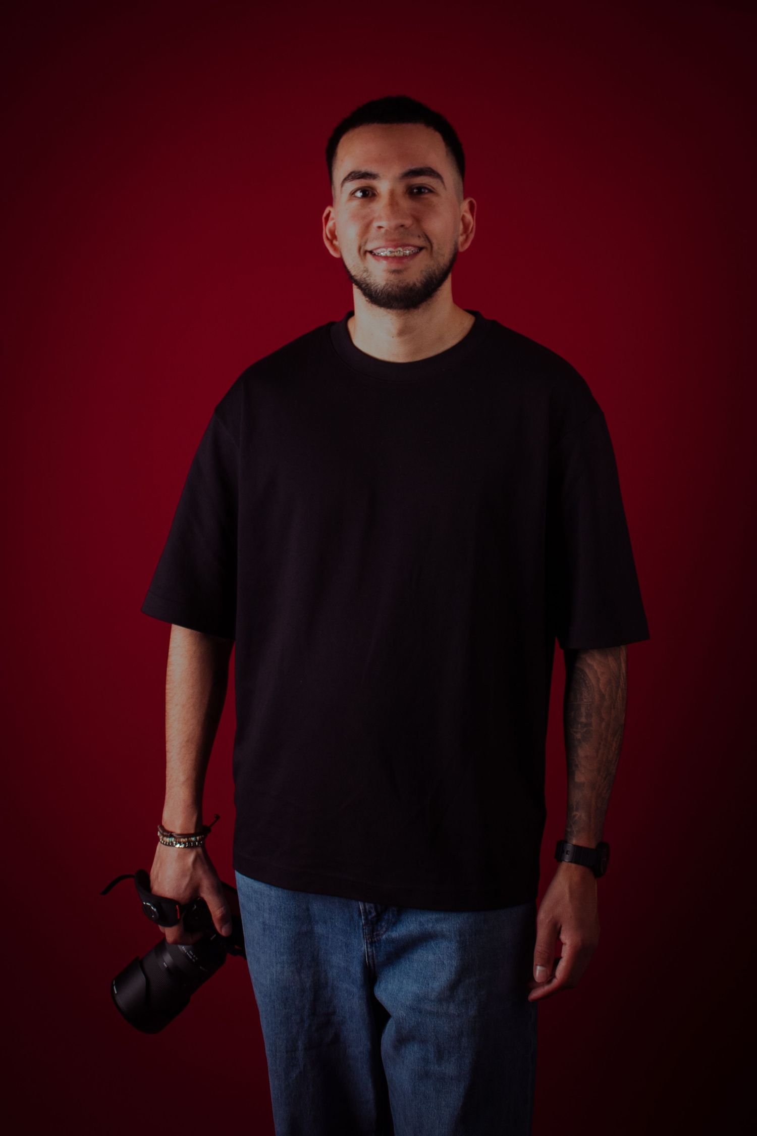 A person wearing a black t-shirt and jeans poses against a dark red background in a series of expressive shots.