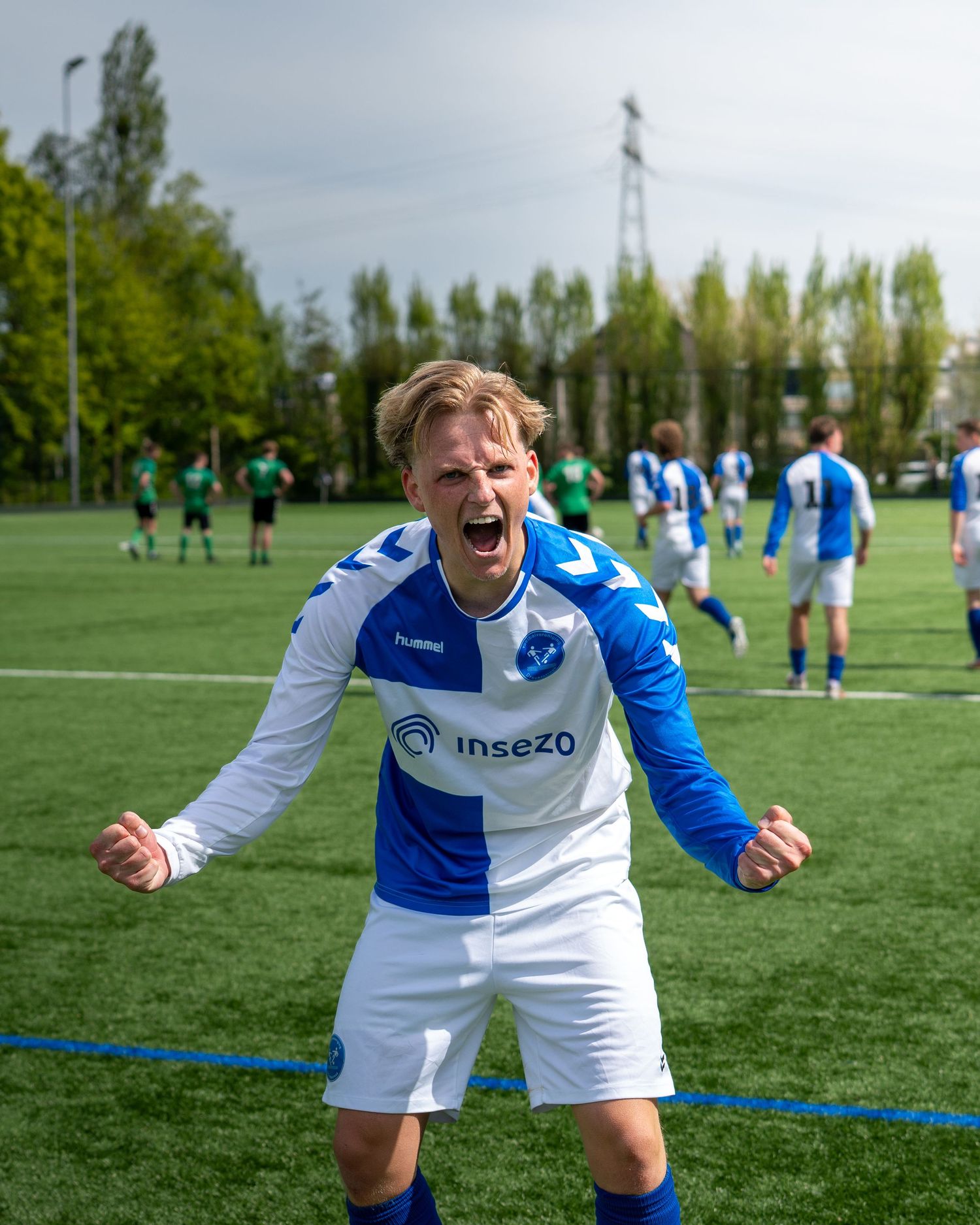 A soccer player in a blue and white Insezo jersey celebrates passionately on a green turf field.
