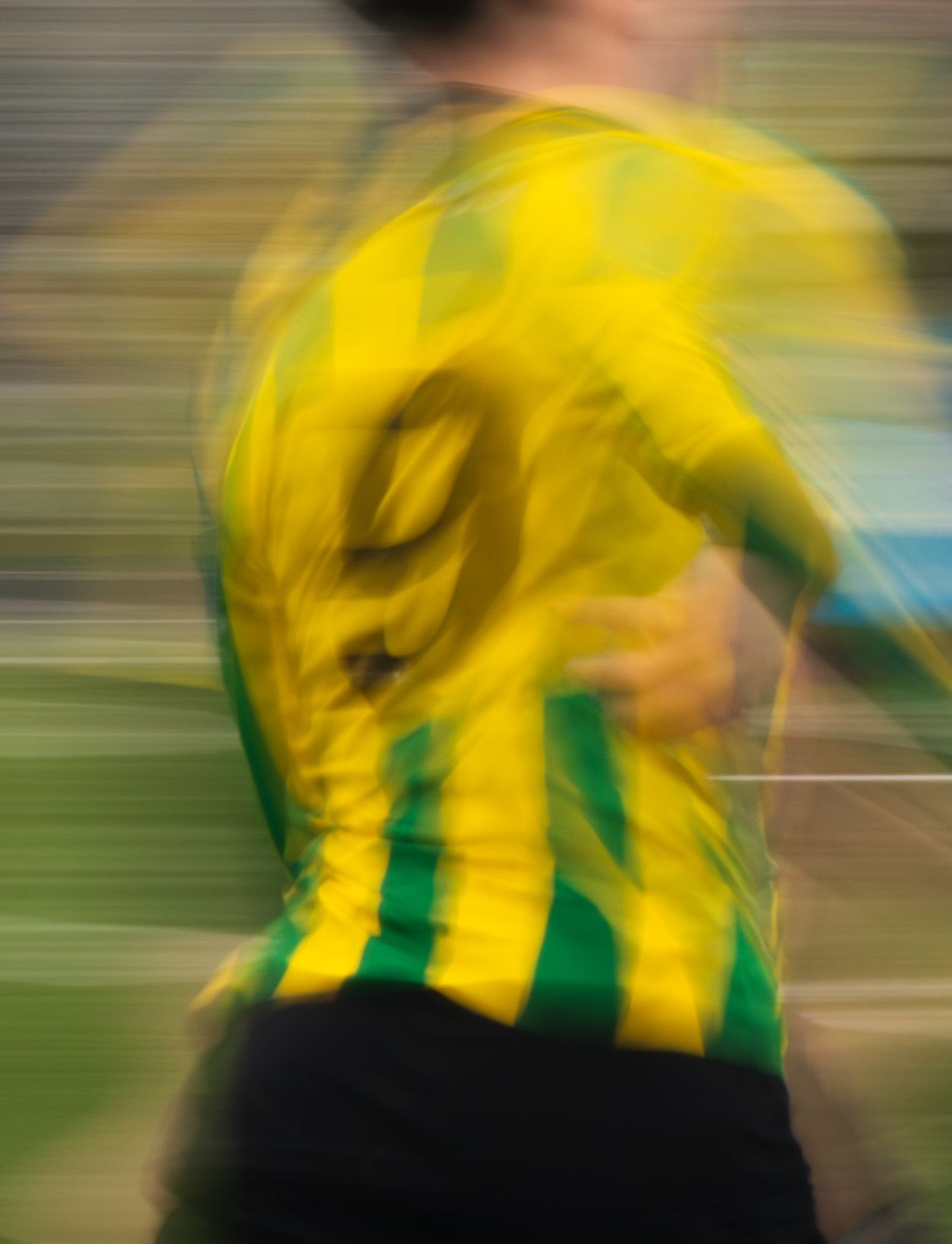 Motion blur effect shows soccer player in yellow and green striped jersey during intense match action.
