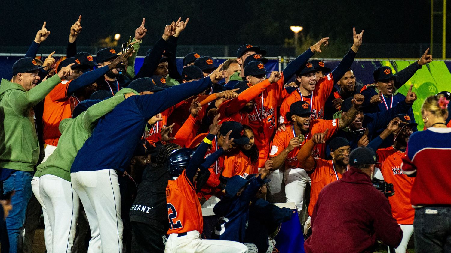Sports fans in orange jerseys celebrate with raised arms and cheering gestures during an exciting game moment.