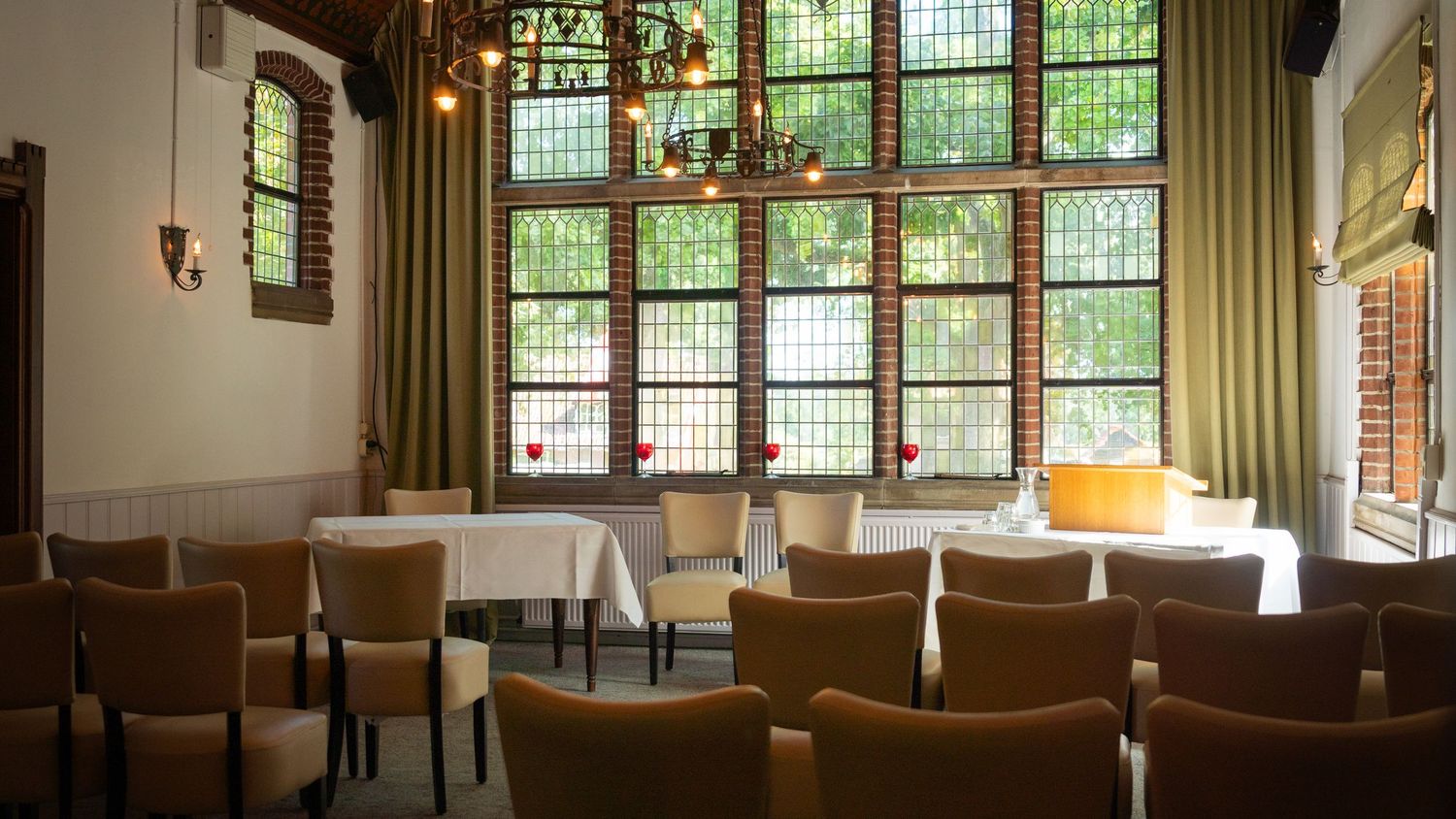 Empty classroom with vintage wooden chairs and large windows with green foliage views at a historic school building.