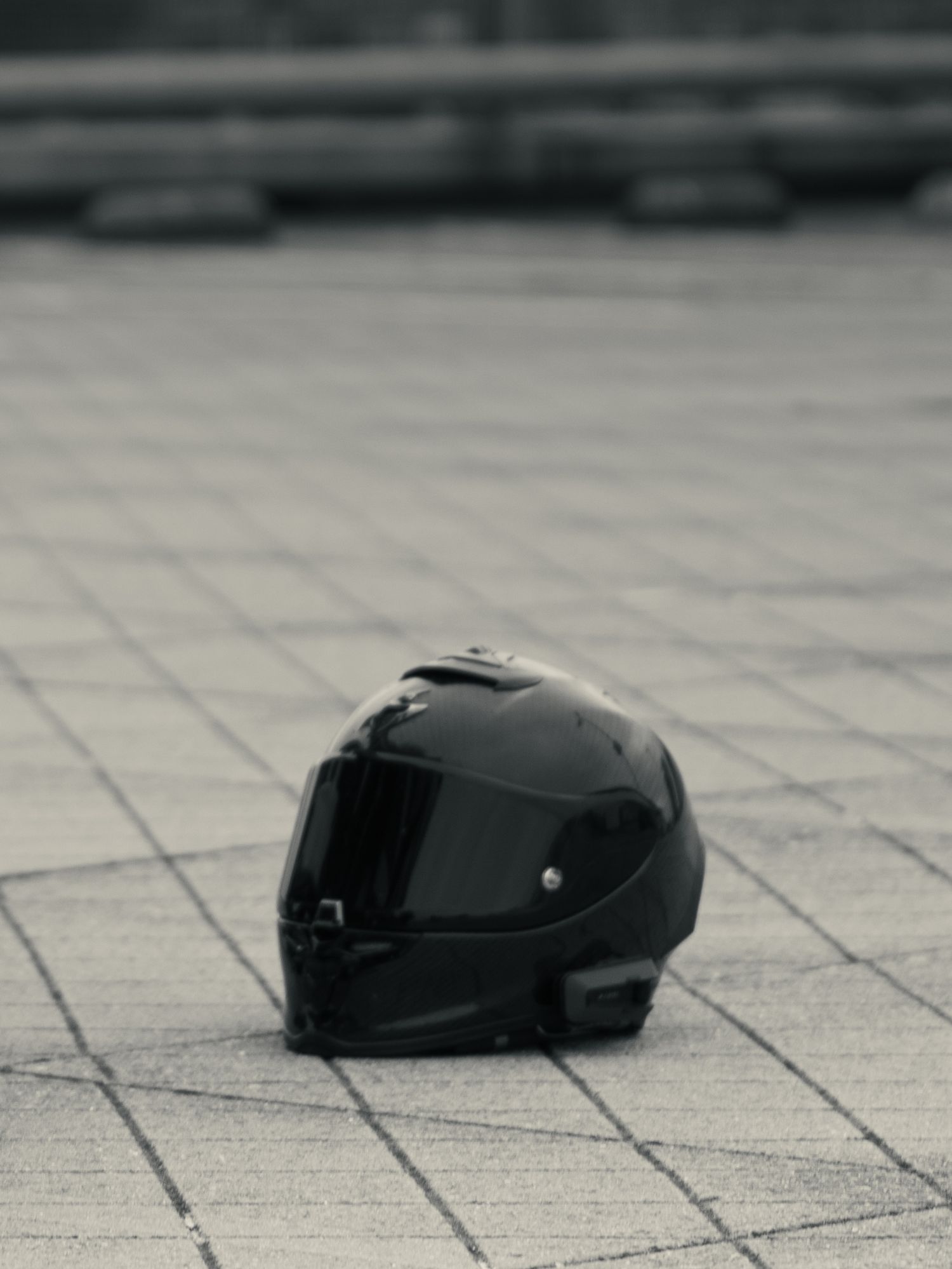 A sleek black motorcycle helmet sits on a gray tiled surface in a minimalist composition.