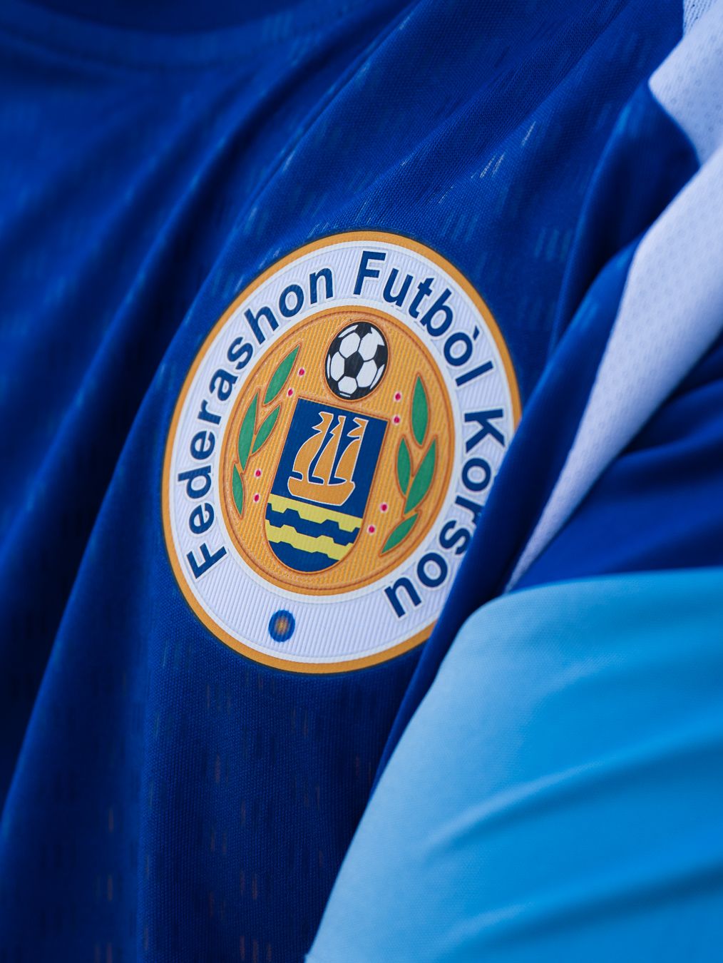 Close-up of Federashon Futbol Korsou official crest on a blue soccer jersey.