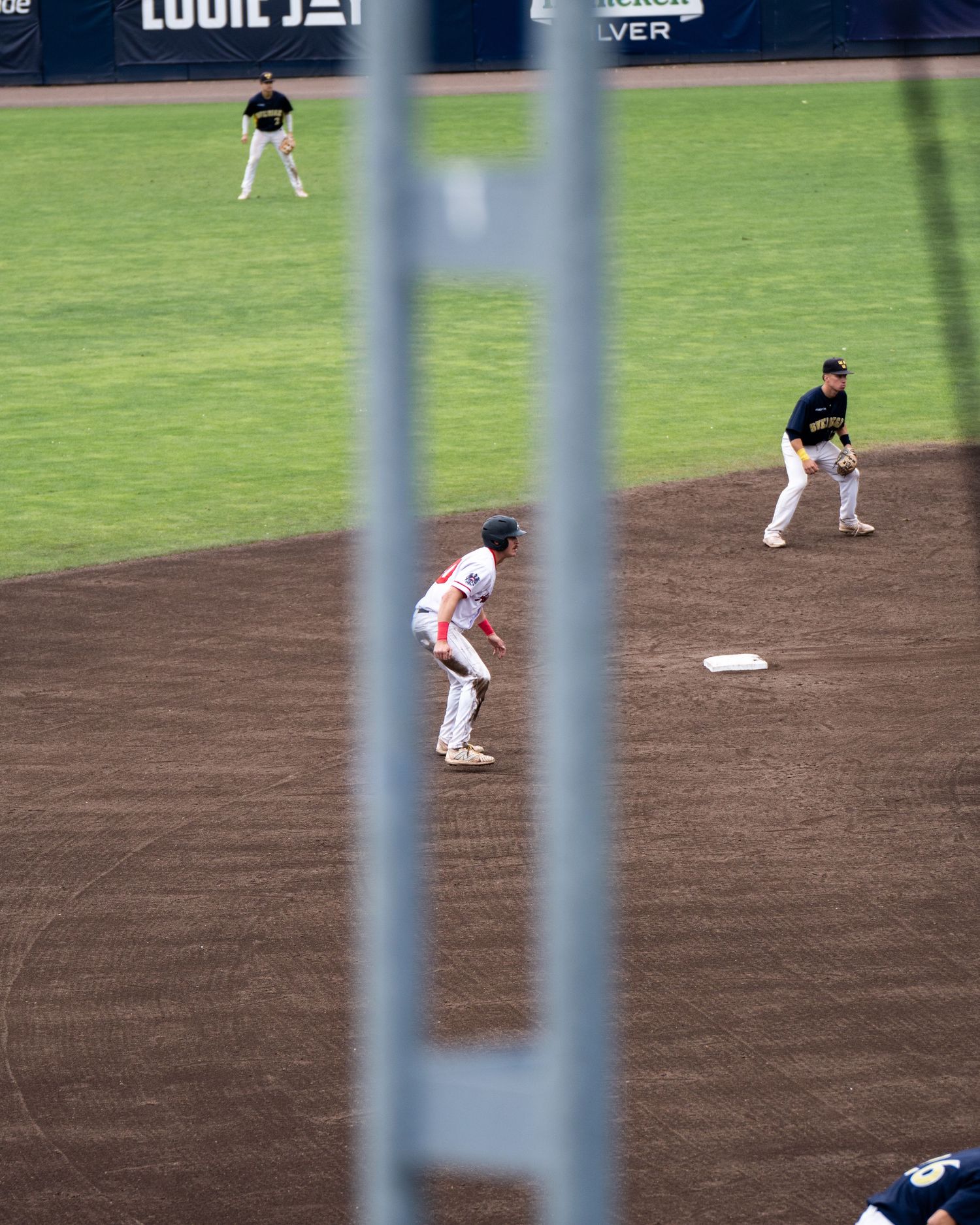 Baseball players positioned on the infield during a game, viewed through stadium railing.