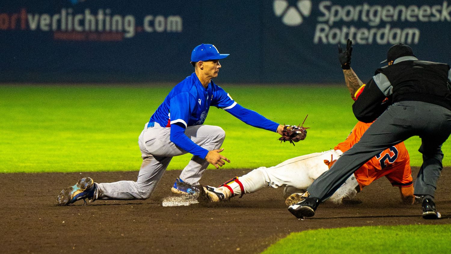 Baseball players in blue uniforms slide into bases during an intense game sequence.