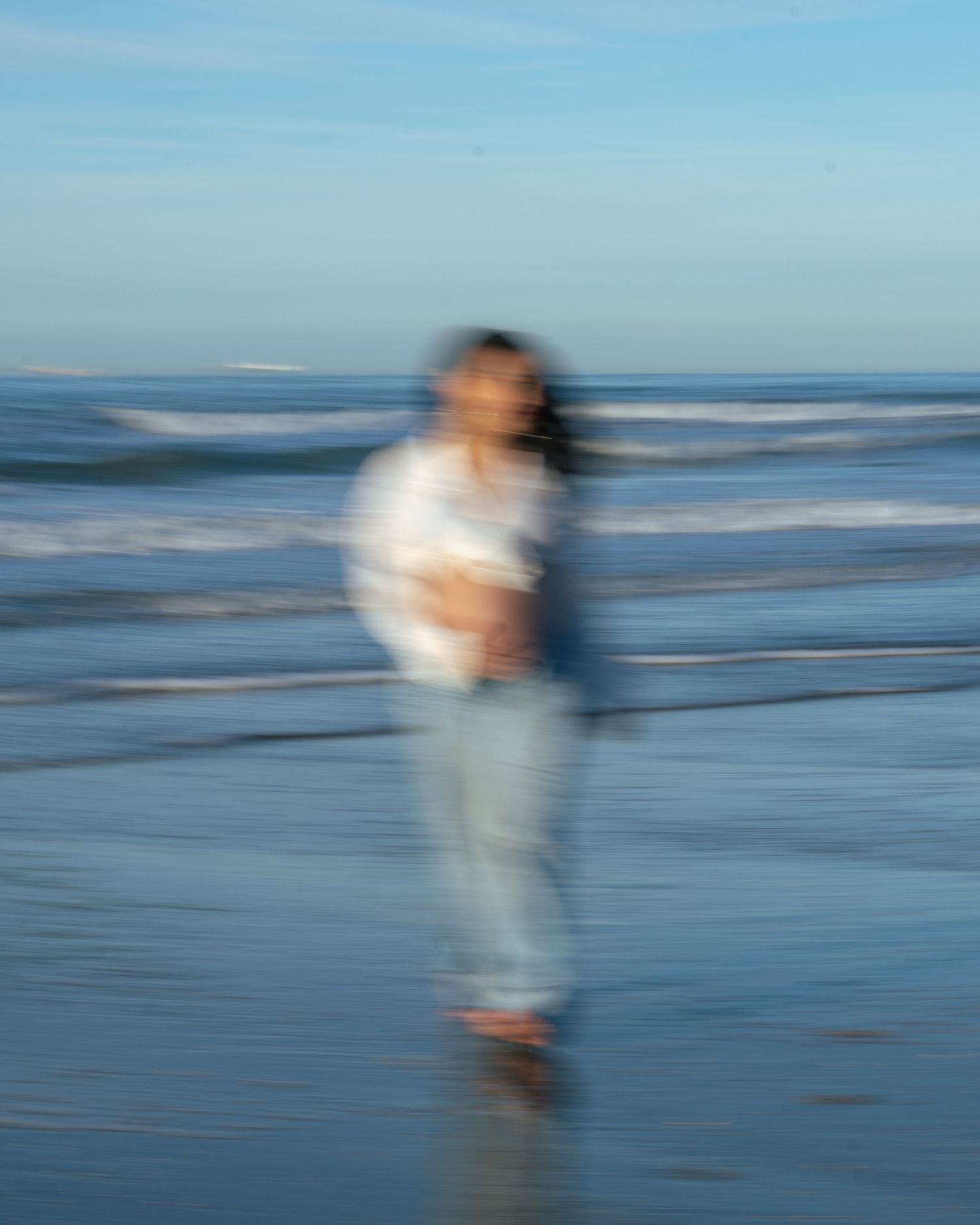 Motion-blurred figure walking along a misty beach shoreline at dusk creates an ethereal silhouette against the ocean.