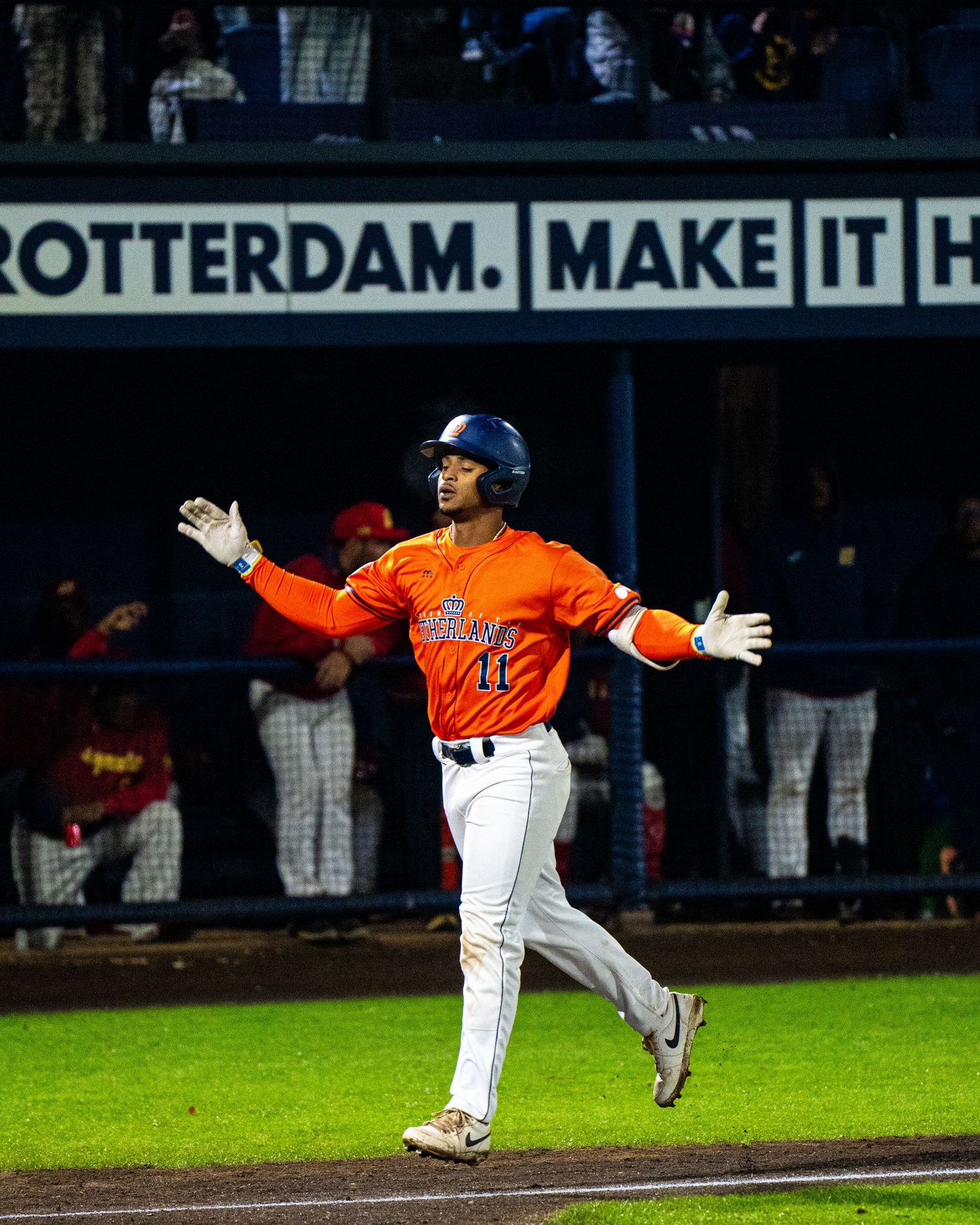 Baseball player in orange jersey makes a diving catch attempt during a night game at the stadium.