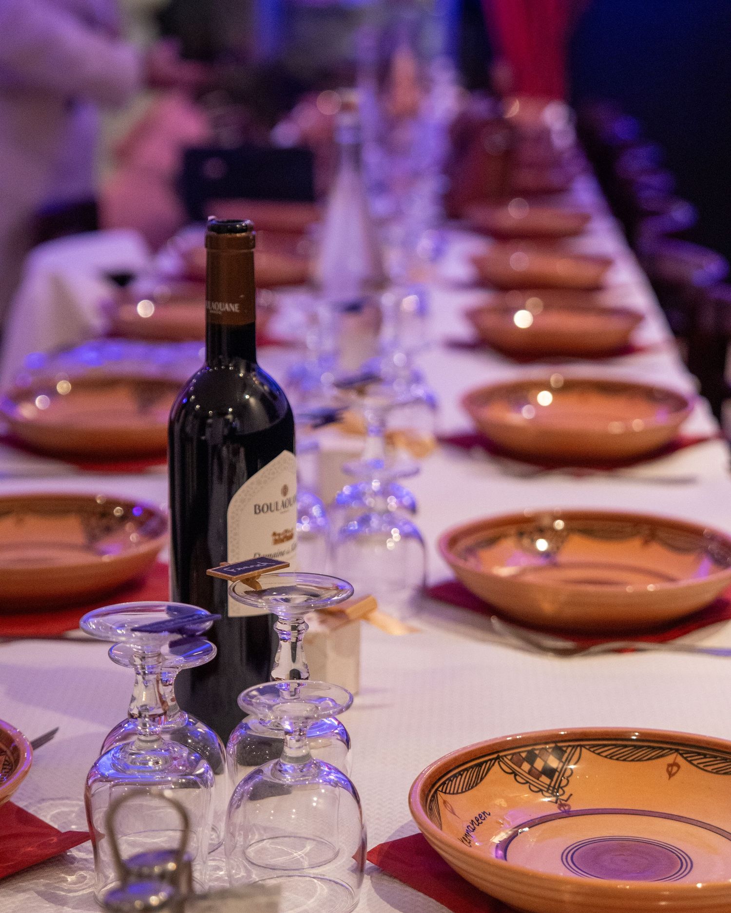 Wine bottle and glasses arranged on an elegant dining table with brown plates and red napkins.