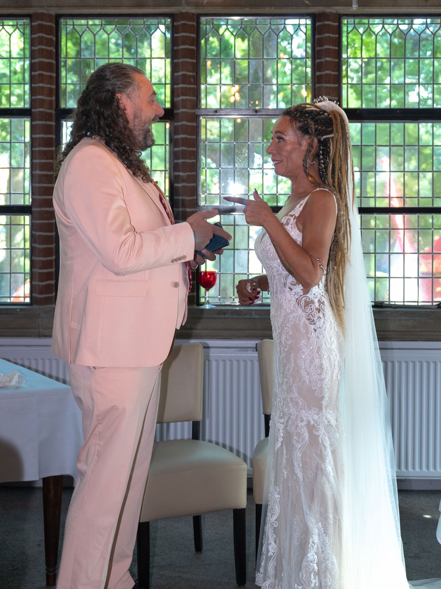 A couple shares a joyful moment during their wedding ceremony in front of bright sunlit windows.