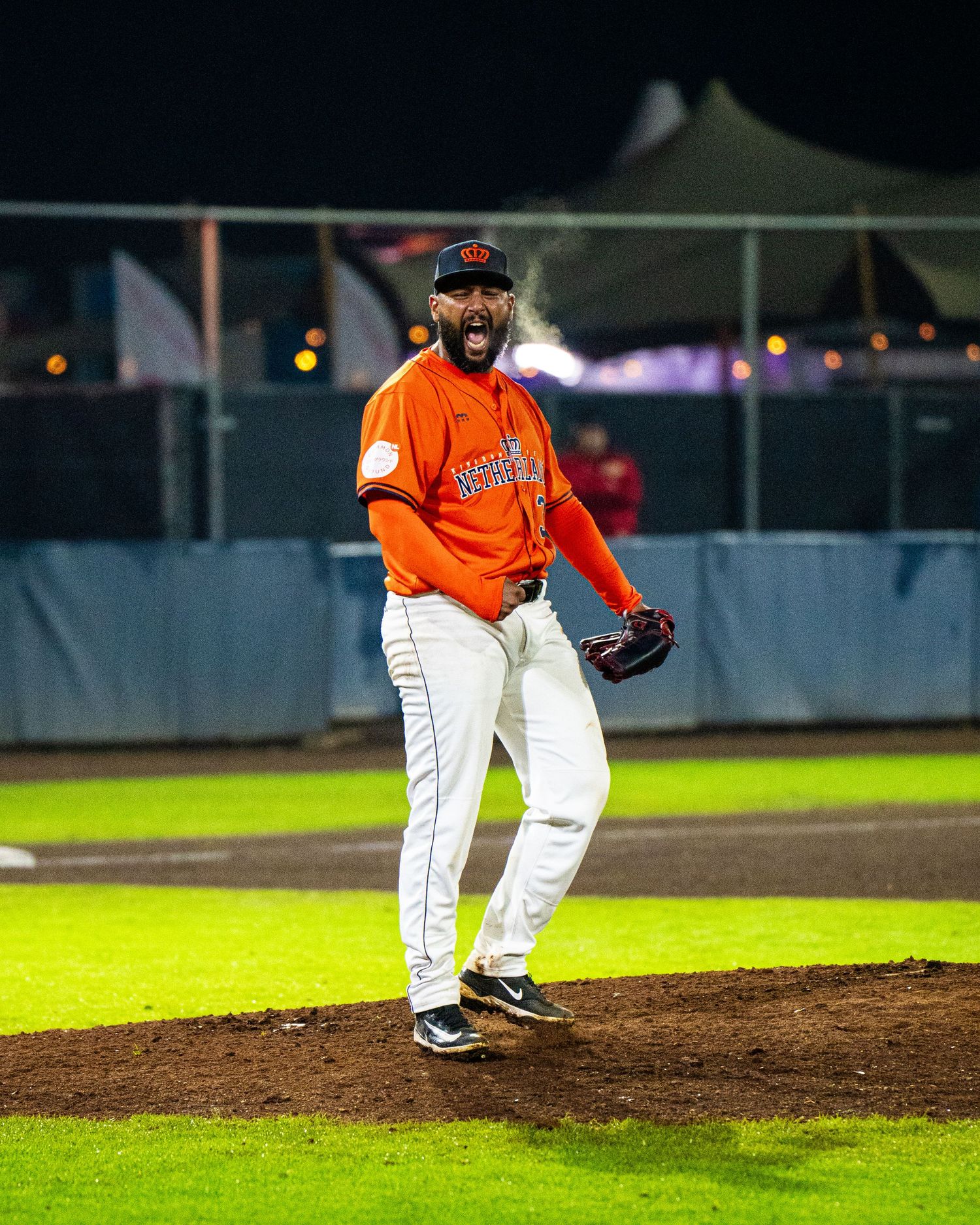 Baseball pitcher in orange uniform winds up to throw from the pitcher's mound during a night game.